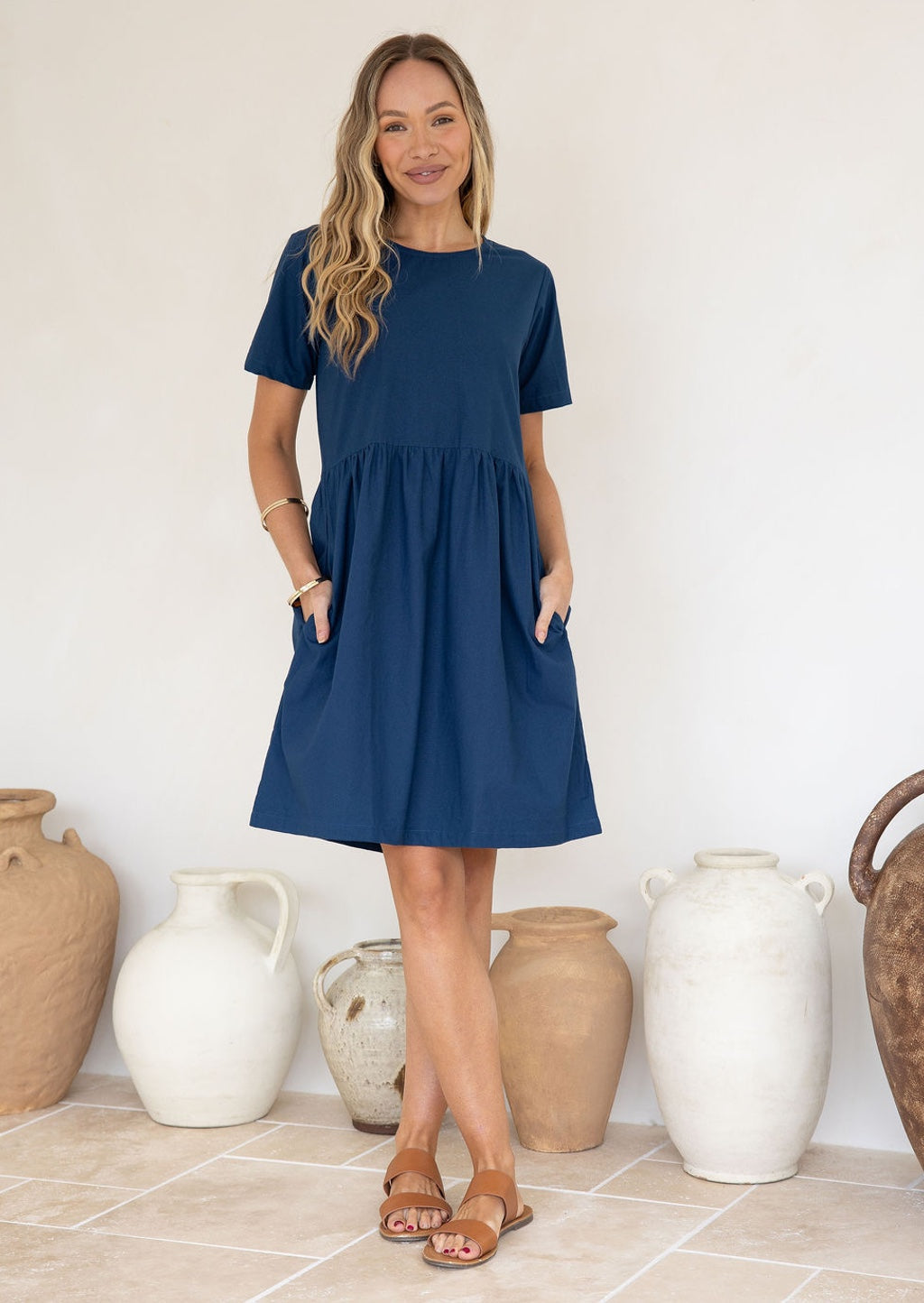 Woman wearing a relaxed fit, above knee length 100% cotton dress with short sleeves, round neckline and hands in pockets