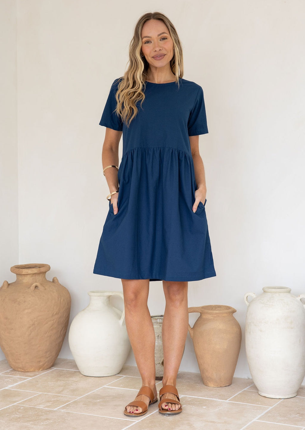 Woman wearing a dark blue, loose fit cotton dress standing in front of decorative vases