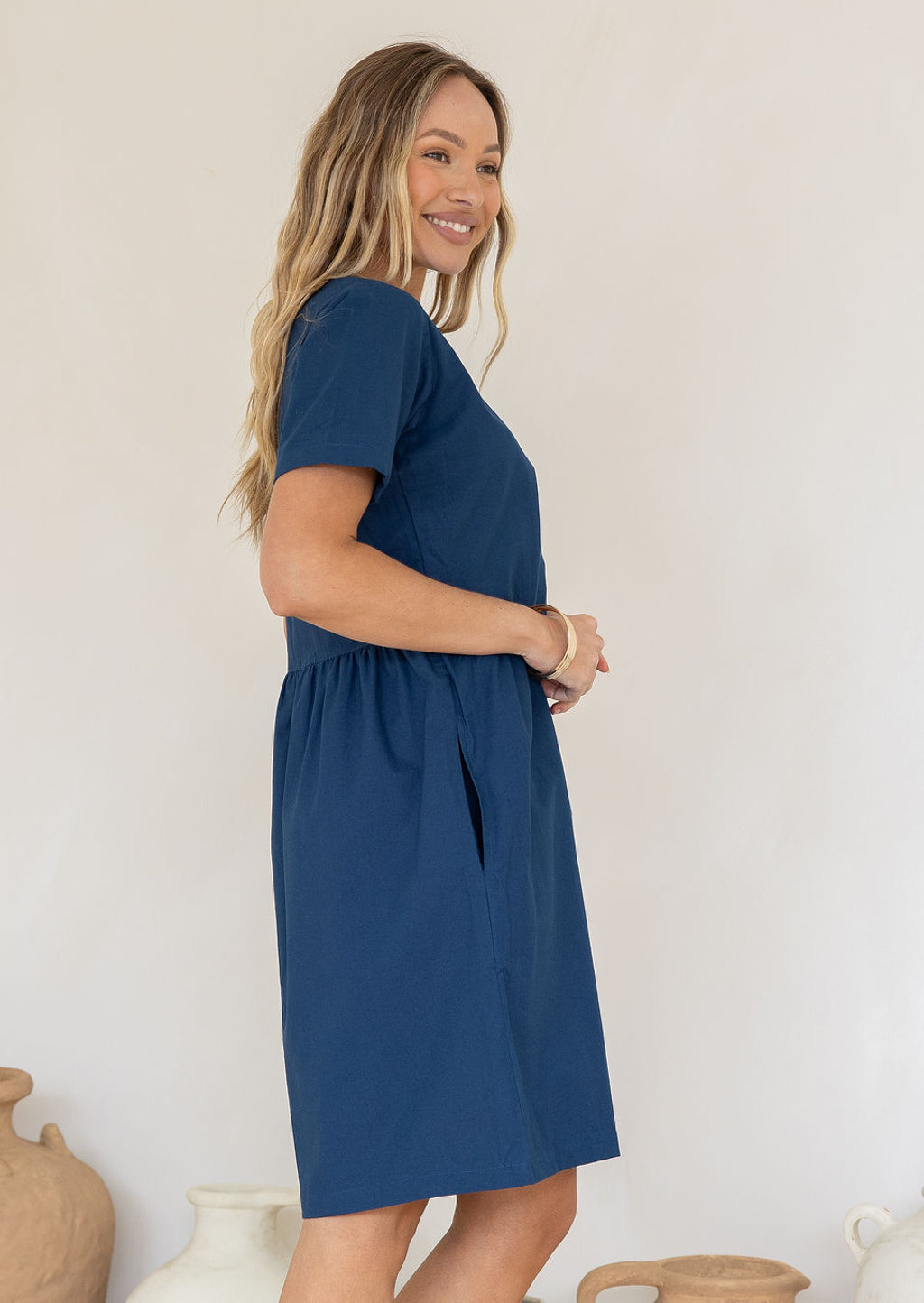 Side pose of model wearing a 100% cotton, short sleeve dress with loose fit, gathers at the waist and pockets