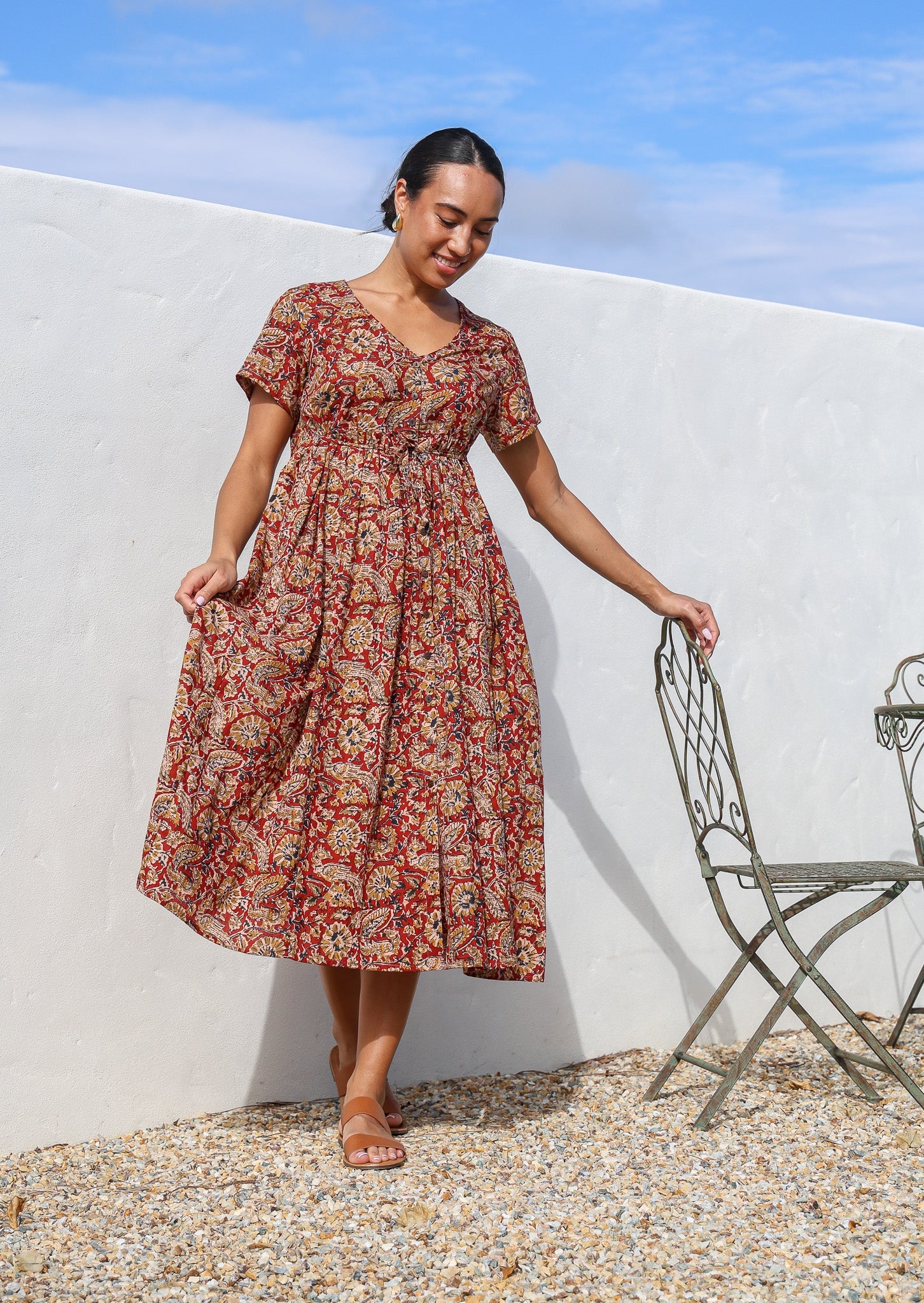 Woman wears lightweight cotton relaxed fit button through red floral dress with hidden side pocket.