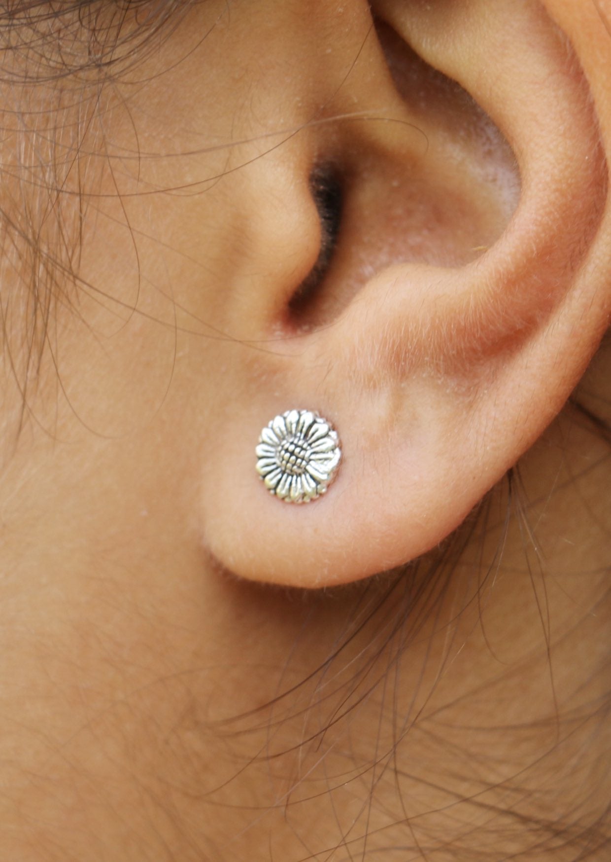 Close up of an ear wearing a sterling silver radiant sunflower studs with textured details