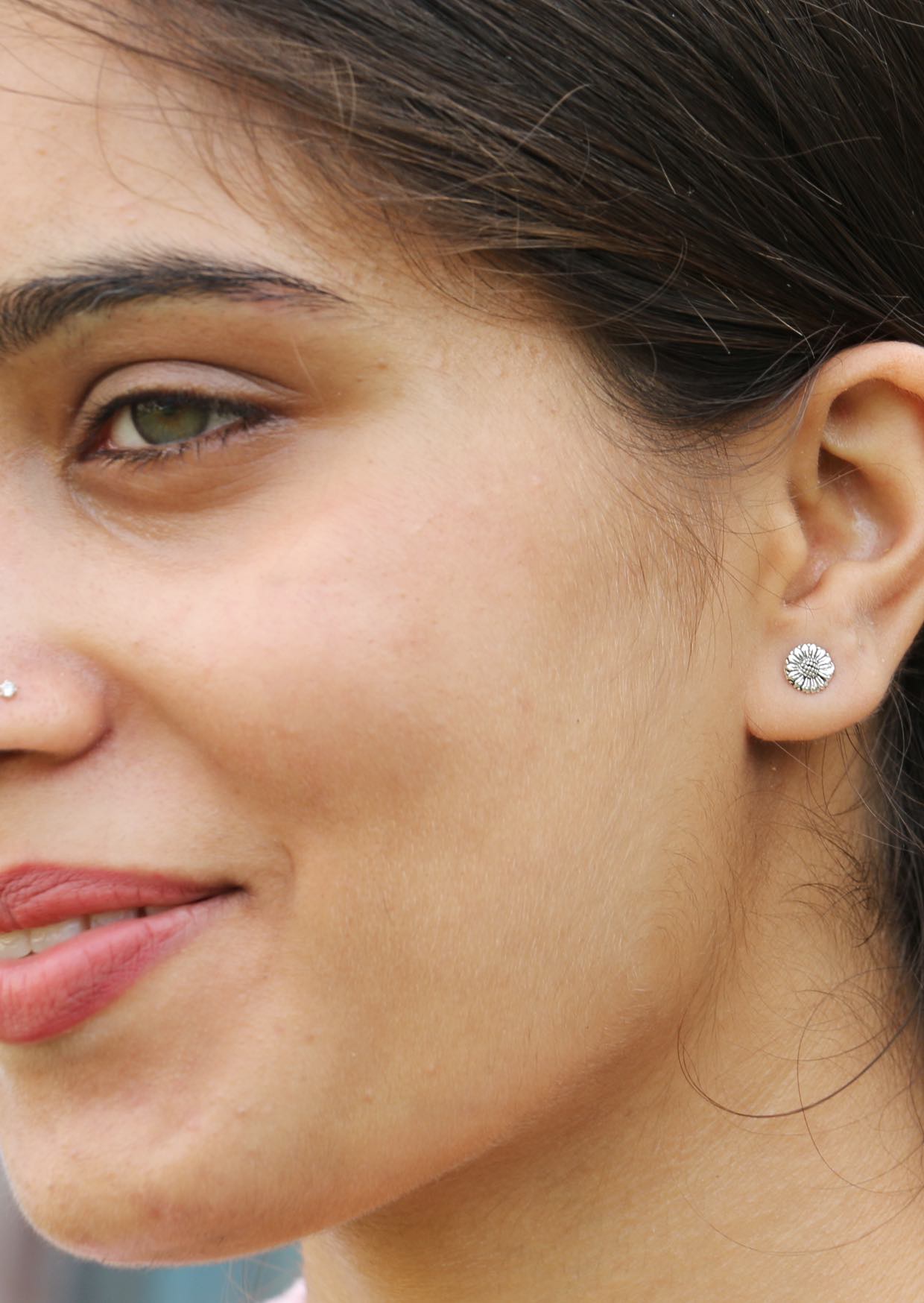 Close-up of a woman wearing textured sterling silver sunflower studs with detailed petals, center and secure butterfly backs