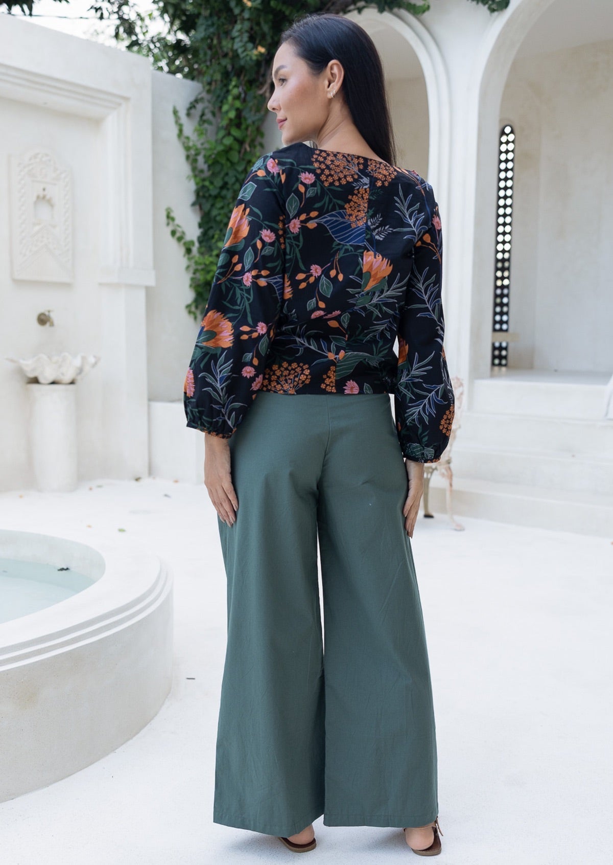 Back view of woman wearing a floral top and green pants with wide legs