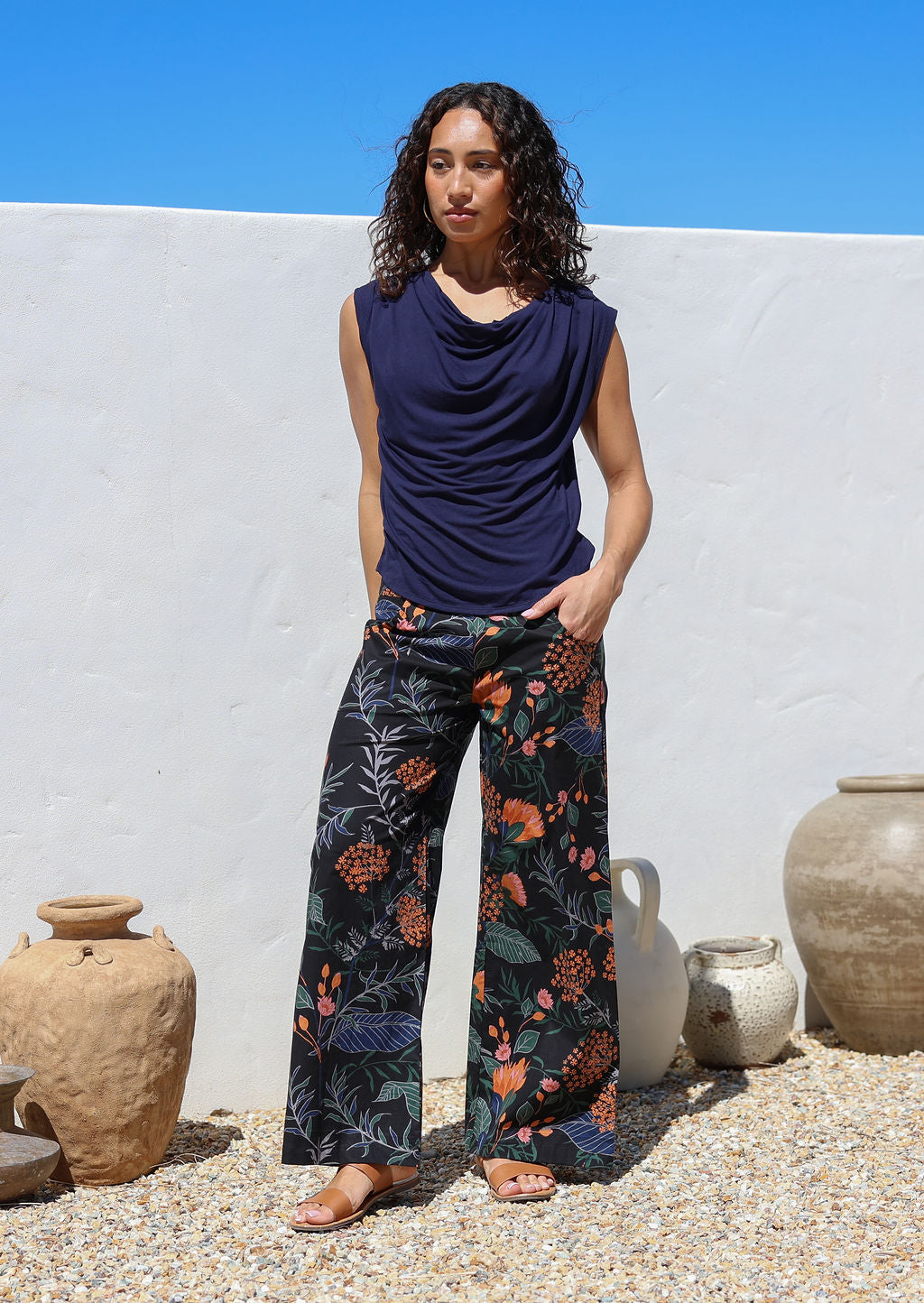 Model with one hand in pants pocket wears black botanical print wide leg cotton pants with pockets and side zip