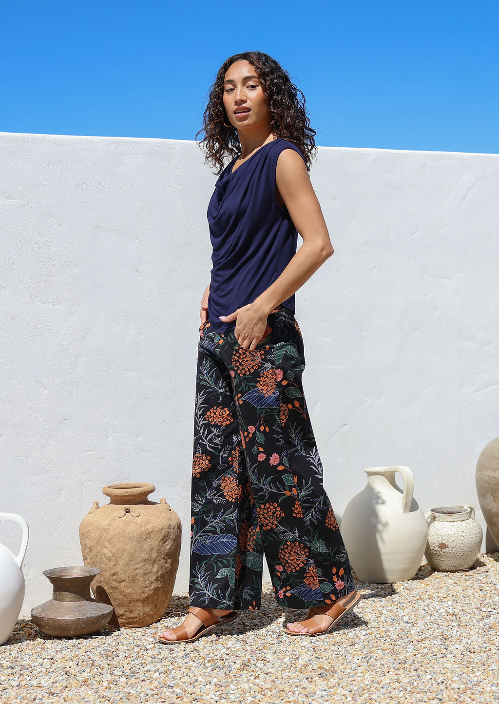 Side pose of model wearing high waisted, wide legged, printed cotton pants in black with pockets and side zipper