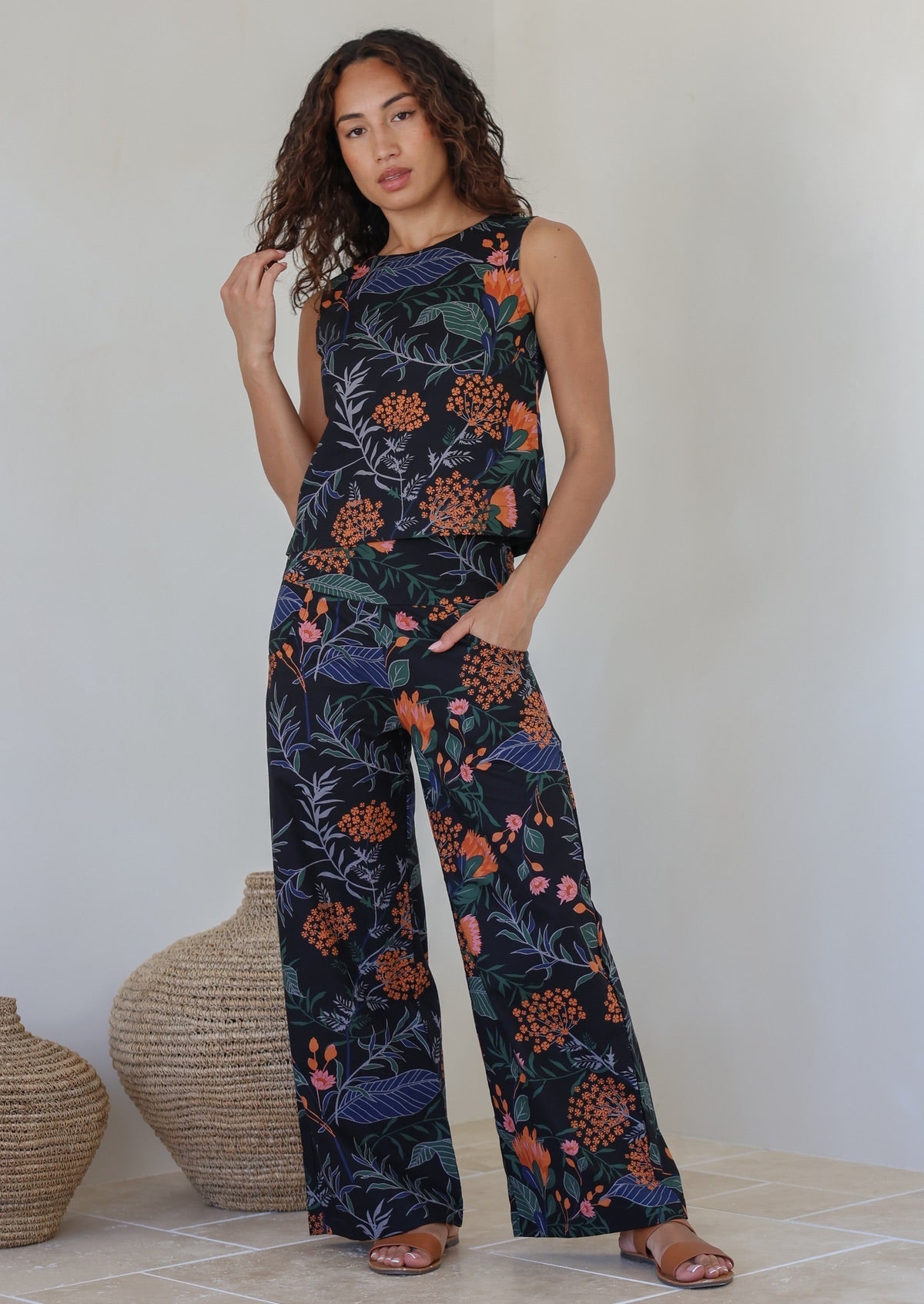 Model wears matching cotton top and pants featuring high waist, side zipper and pockets in dark based botanical print
