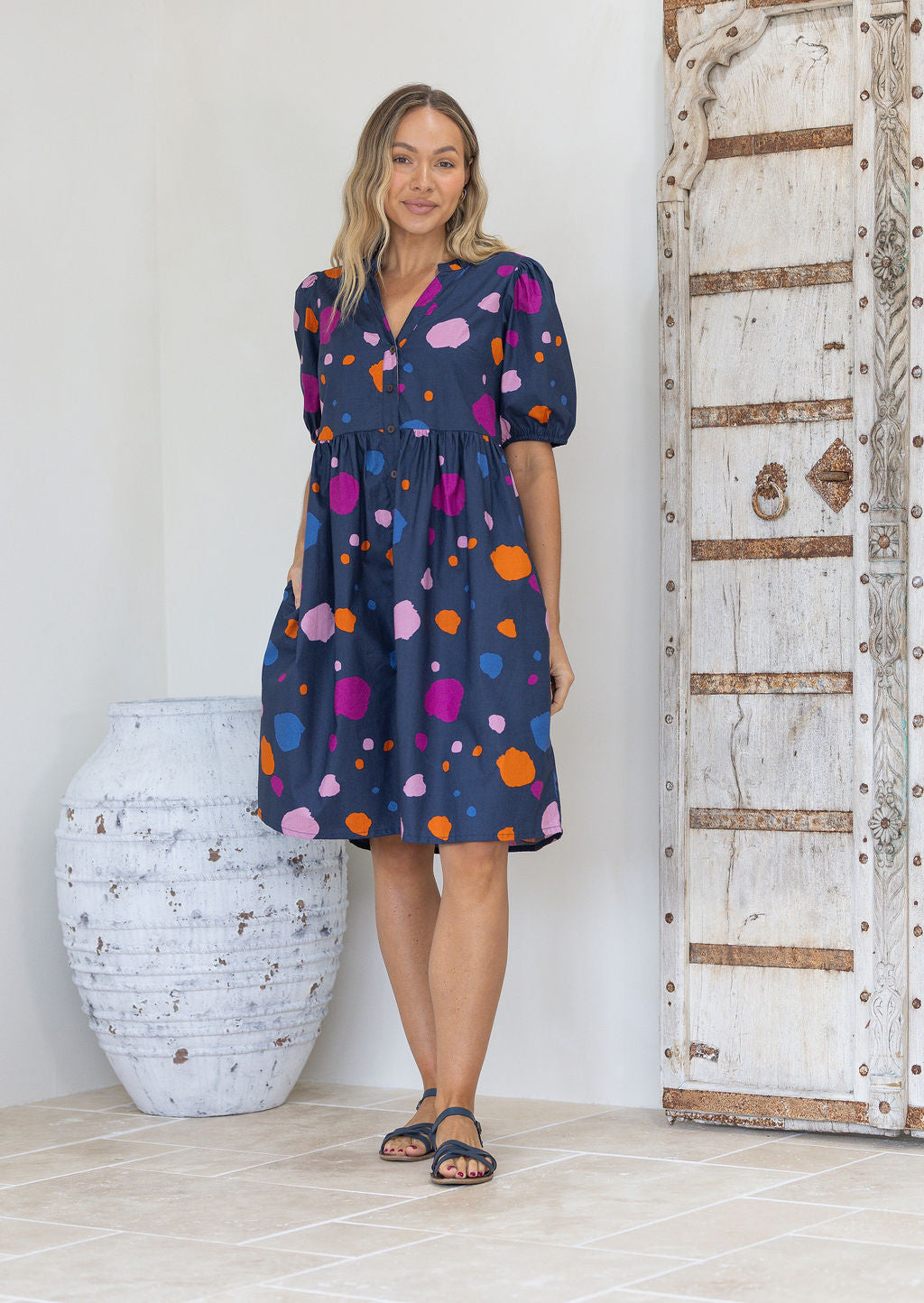 Woman wearing a colourful polka dot on a blue base cotton button through babydoll dress