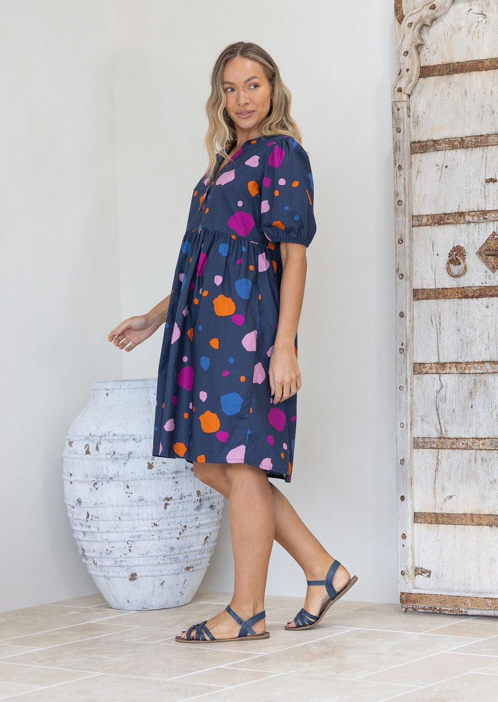 Woman wearing a navy dress with colourful polka dots, relaxed fit empire waistline and elasticated elbow length sleeves