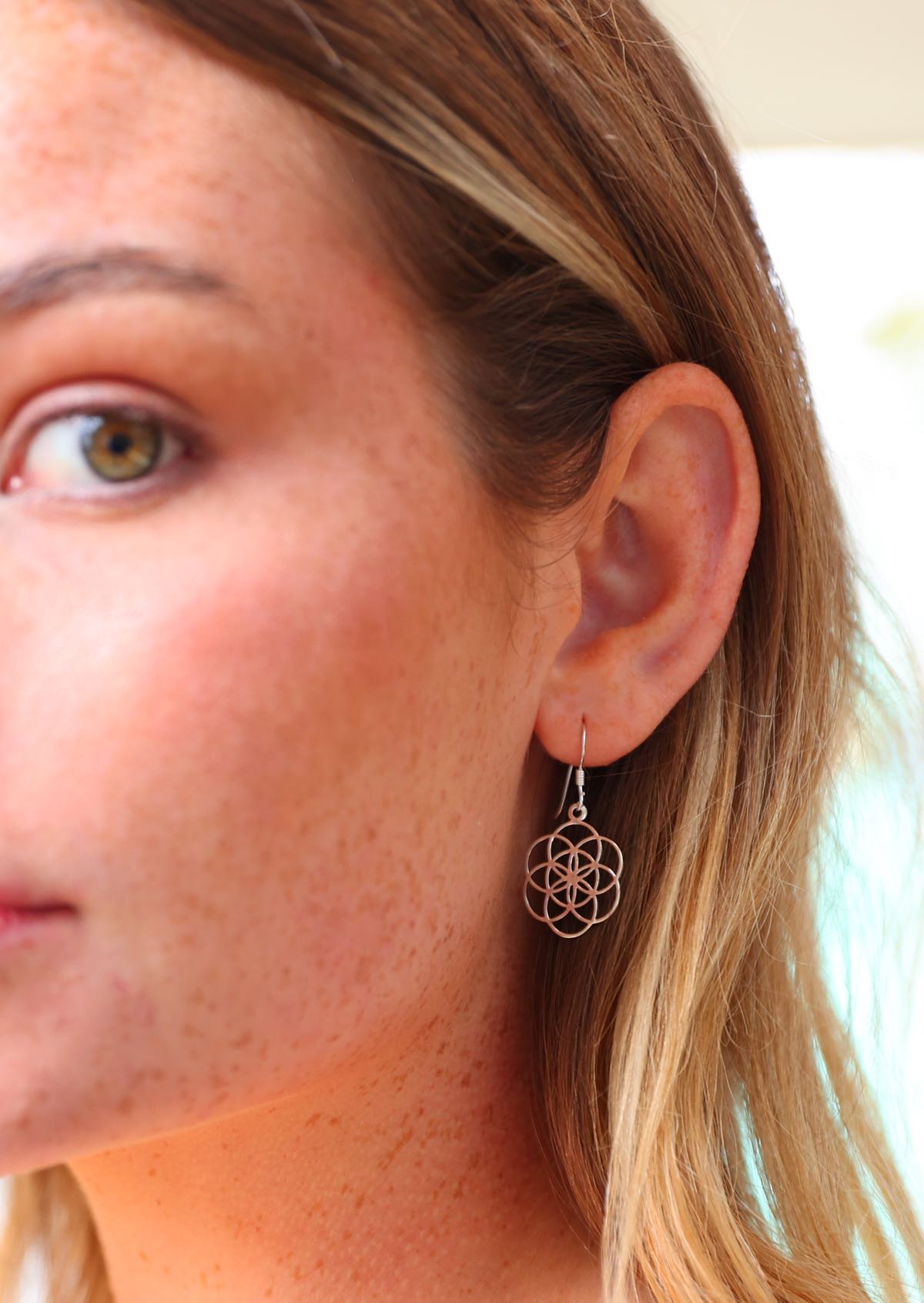 Woman wears silver hook earrings with sacred geometry of seven intersecting circles