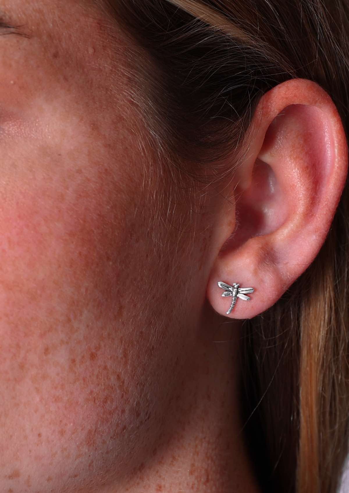 Close up of small sterling silver dragonfly stud earrings in model's ear