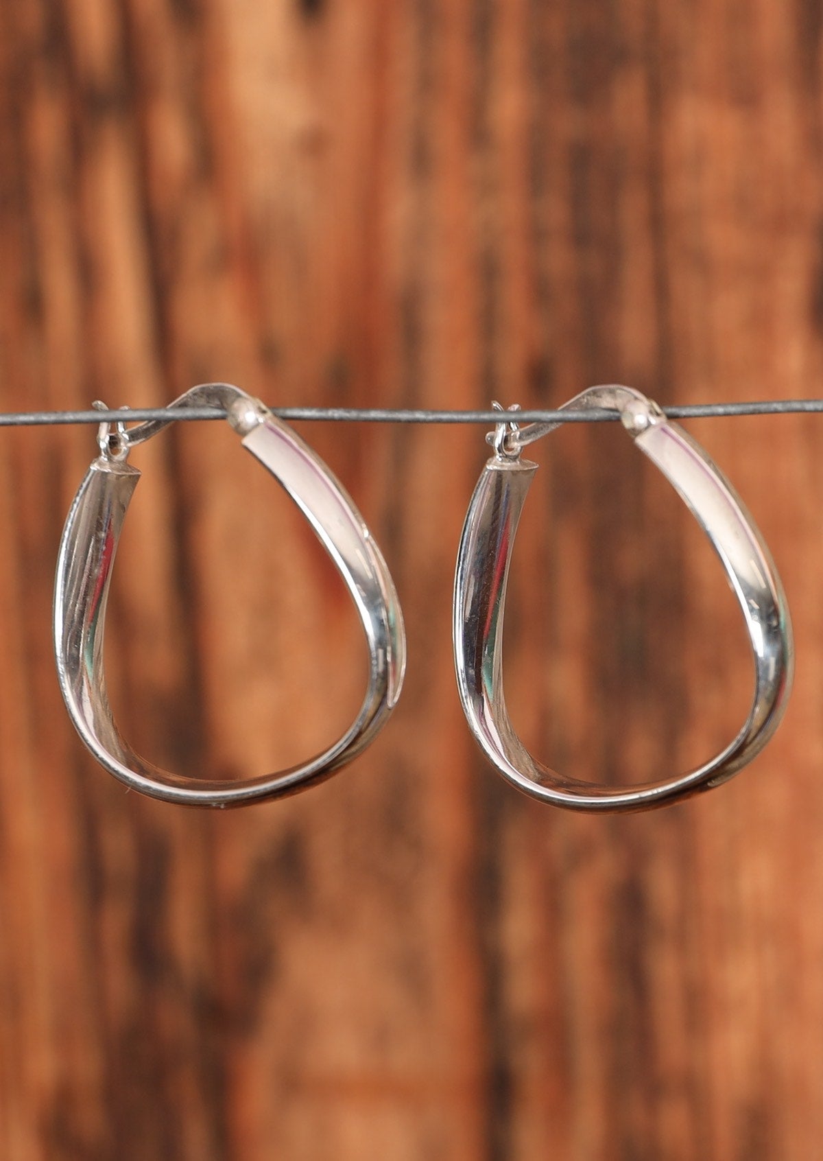 92.5% silver abstract hoop earrings placed on a wire for display.