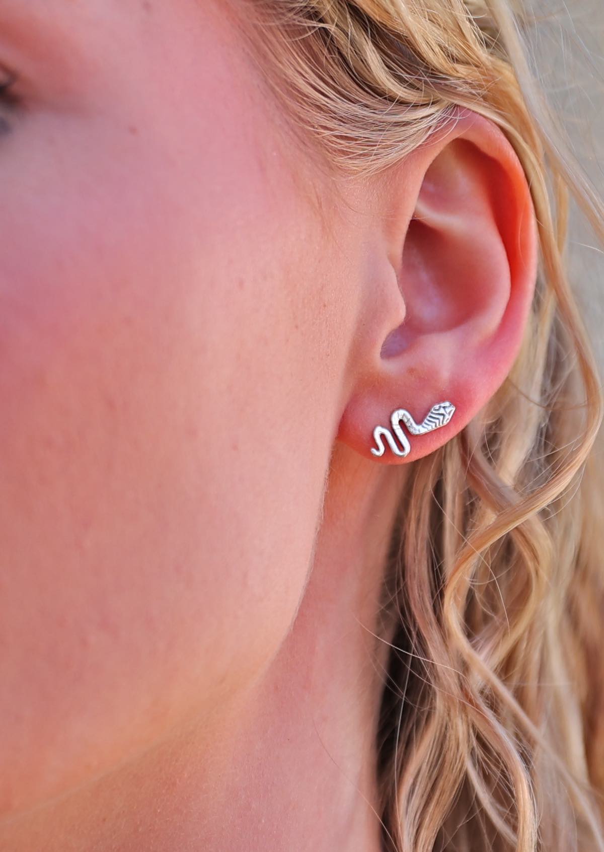 A person wearing silver snake stud earrings with a flowing, curvy shape.