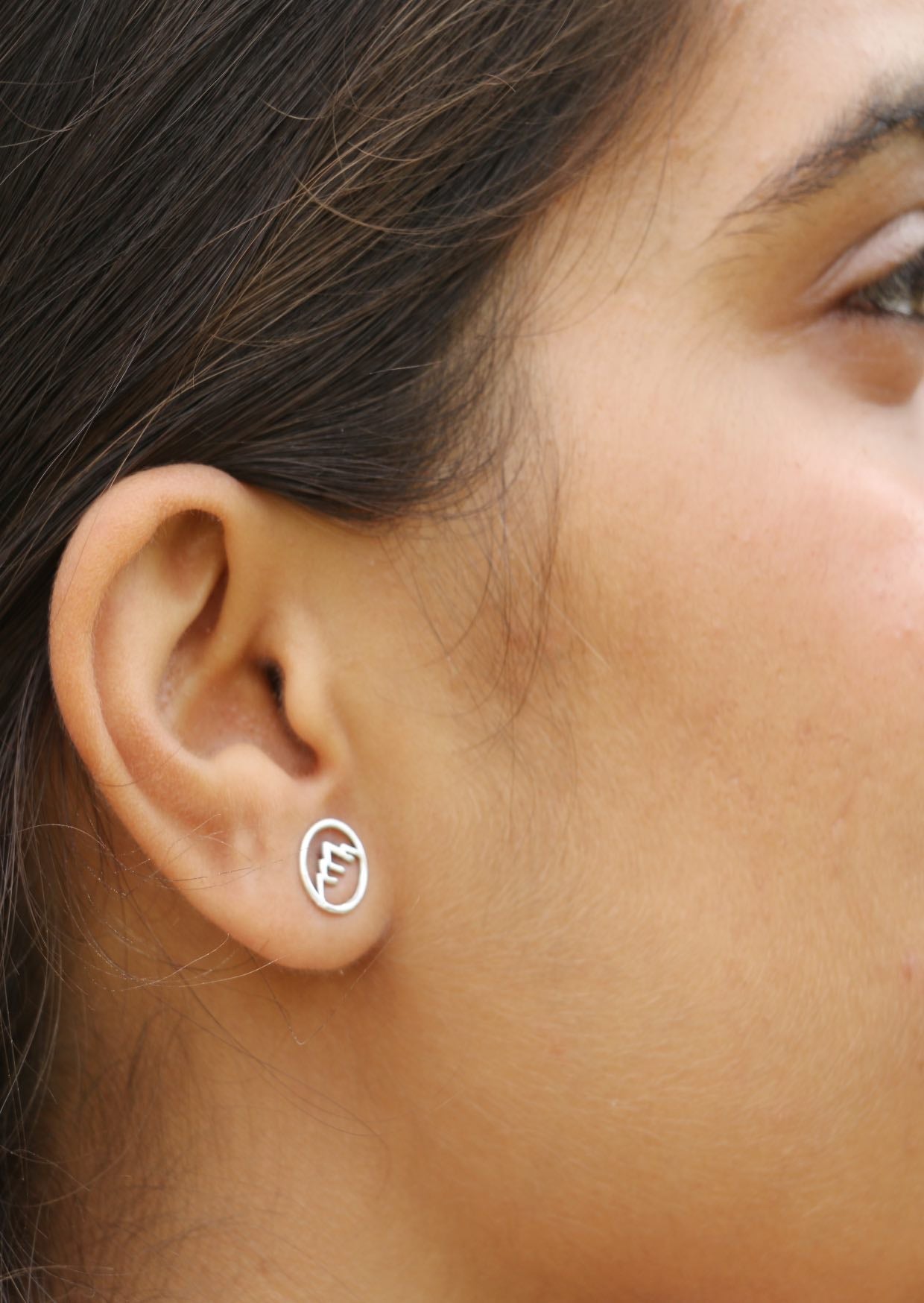 Close-up of an ear wearing a silver circular Alps studs with delicate mountain cutout details