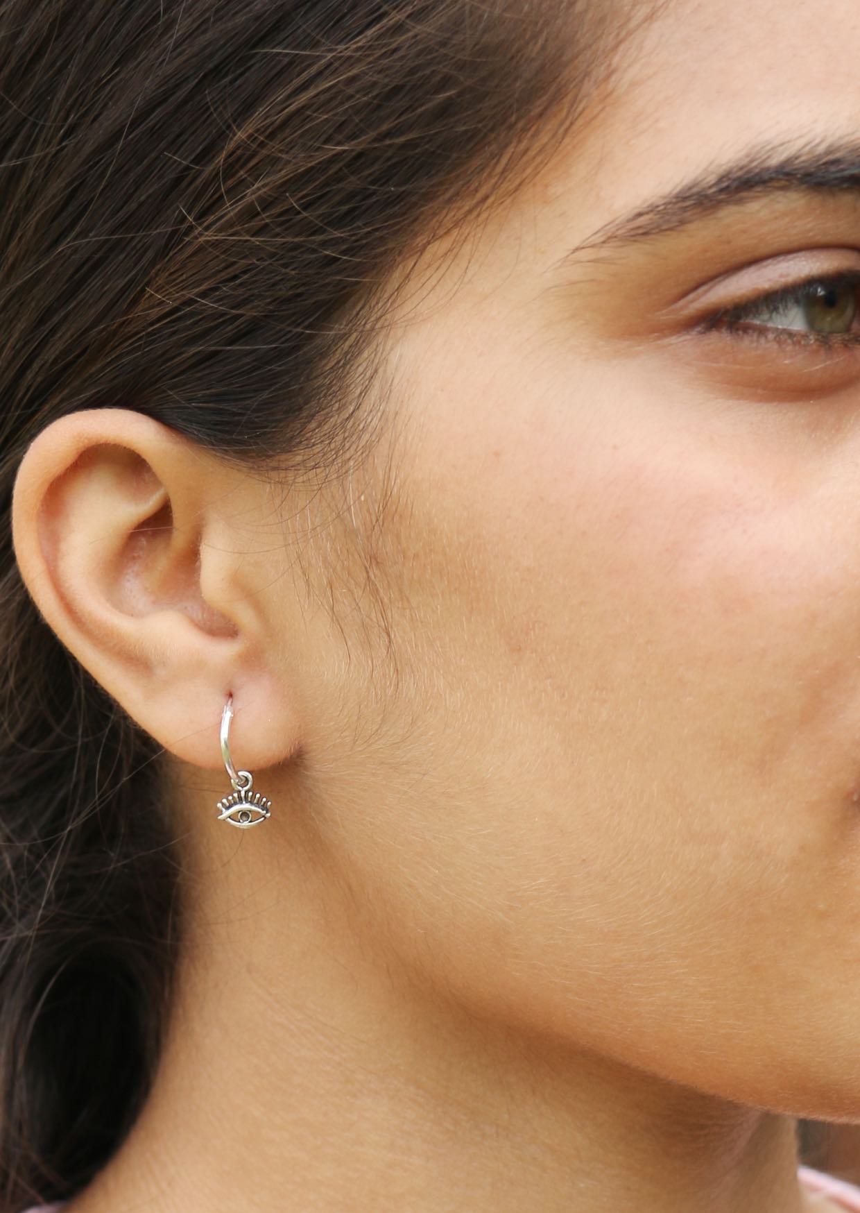 Woman wearing silver hoop earring with delicate eye shaped charm