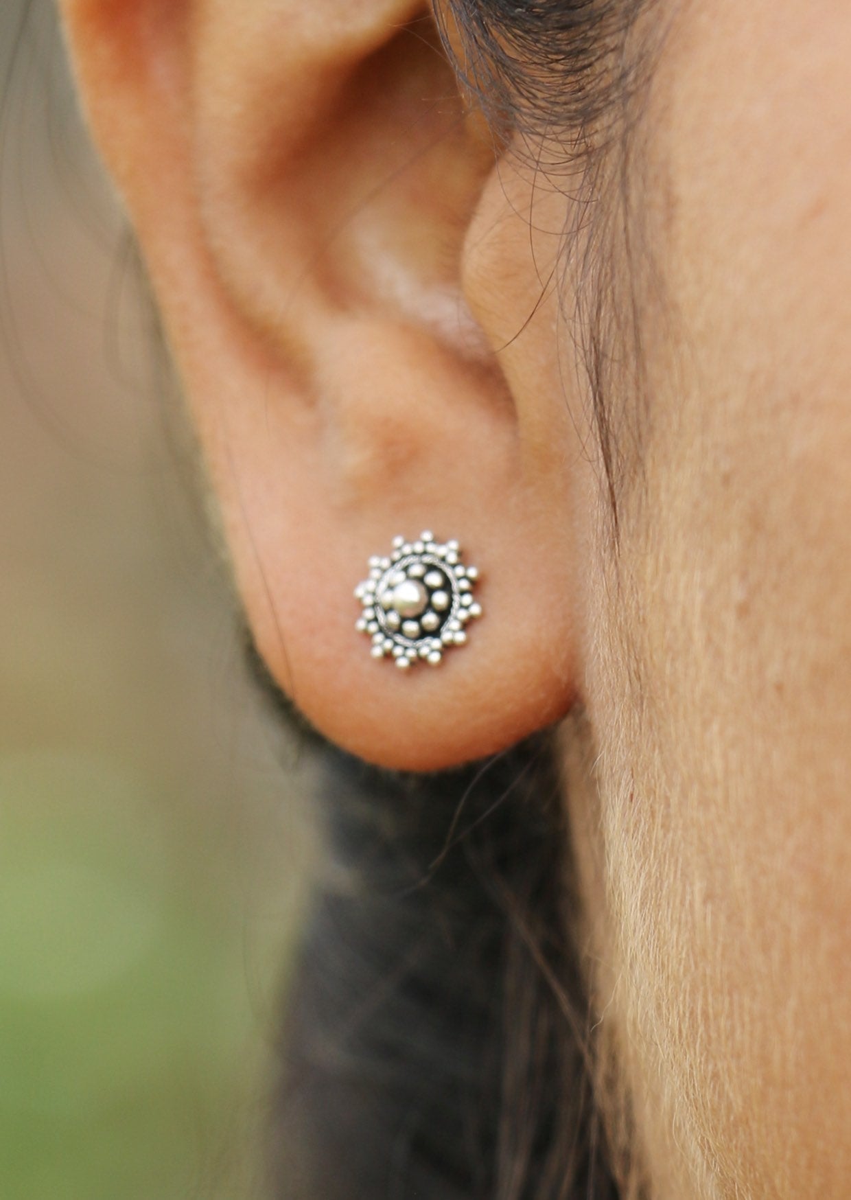 Silver ornate circular studs with a beautiful intricate design and butterfly backs, displayed on a woman’s ear