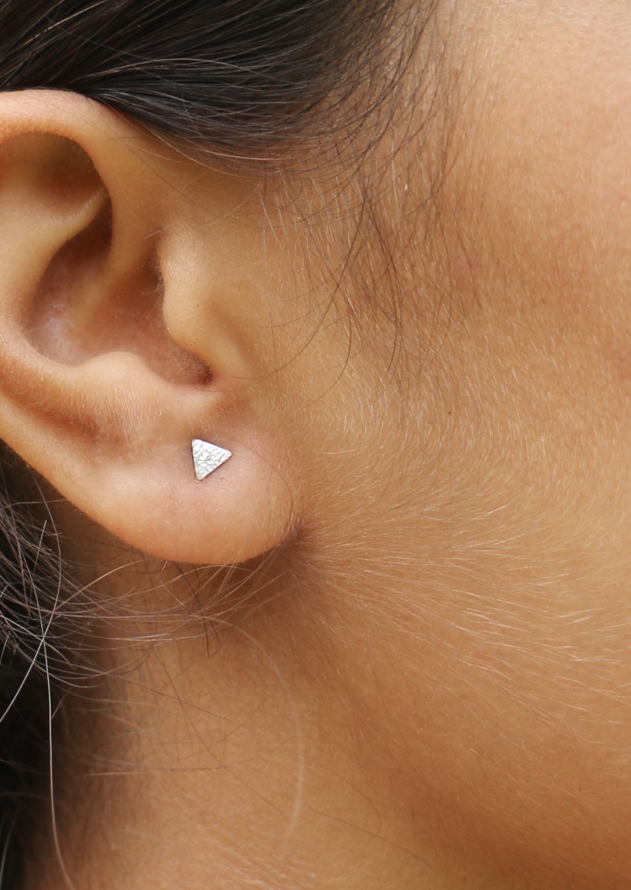 Close-up of an ear adorned with small textured silver triangular studs secured by butterfly backs