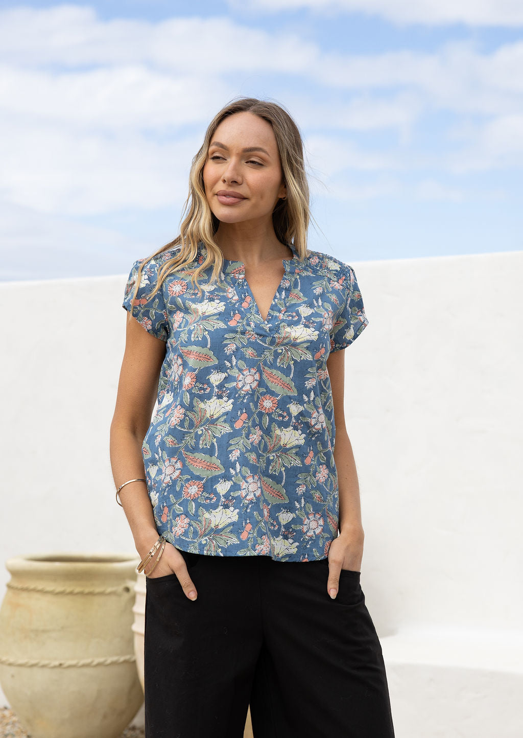 Woman wearing a cotton dusty blue floral print short sleeve blouse with V-neckline and elastic ruching at the front of the shoulders