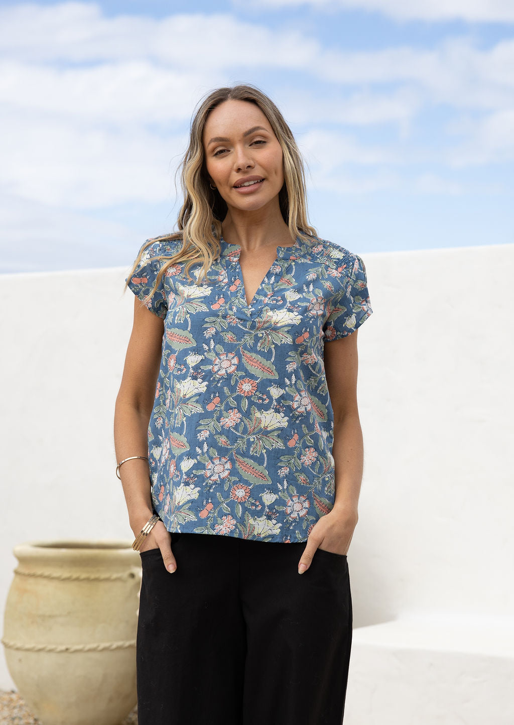 Woman wearing a floral cotton blouse with ruched shoulder and V neckline paired with black cotton pants.