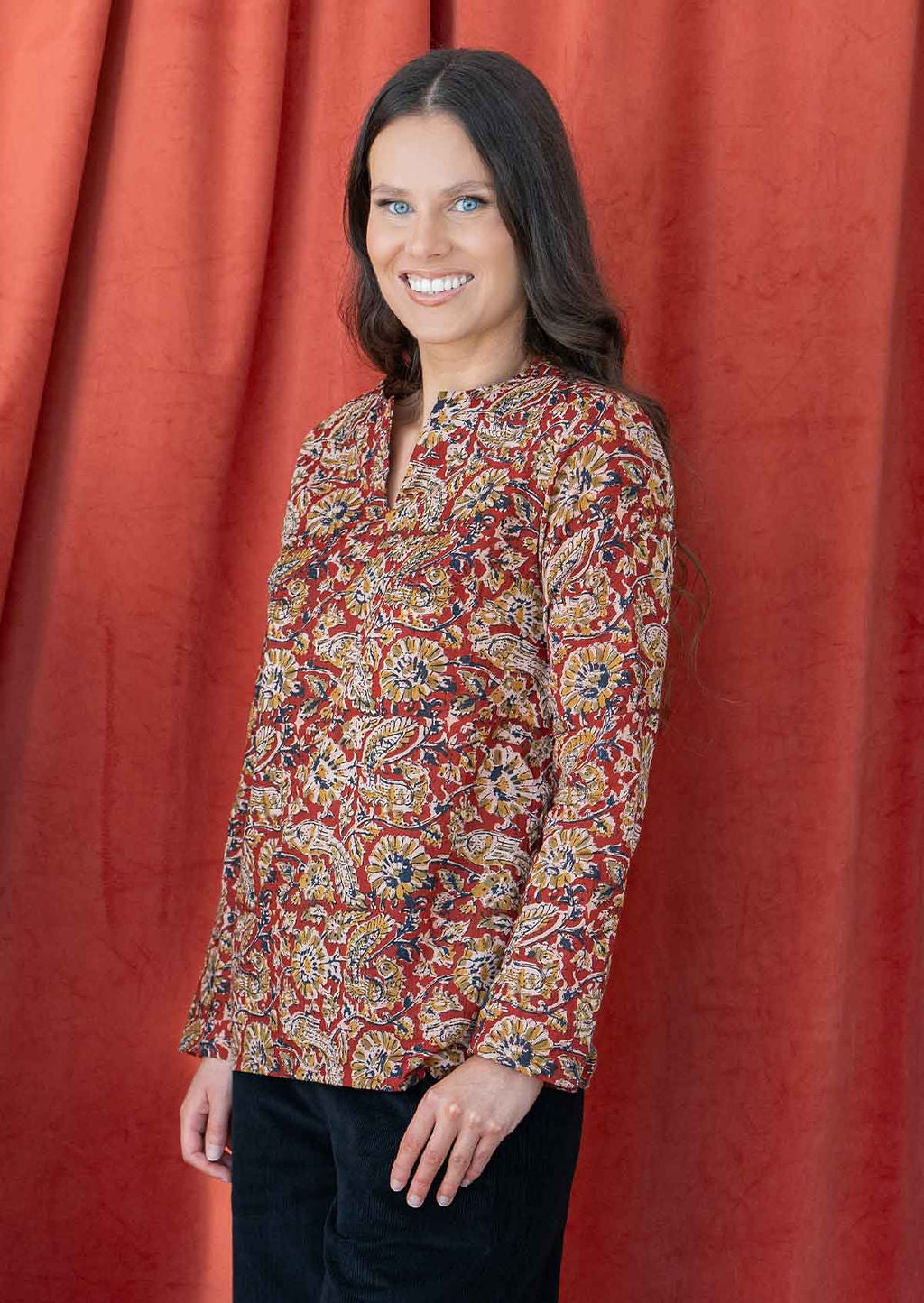 Model poses side in long sleeve cotton top in delicate floral print on a rust base