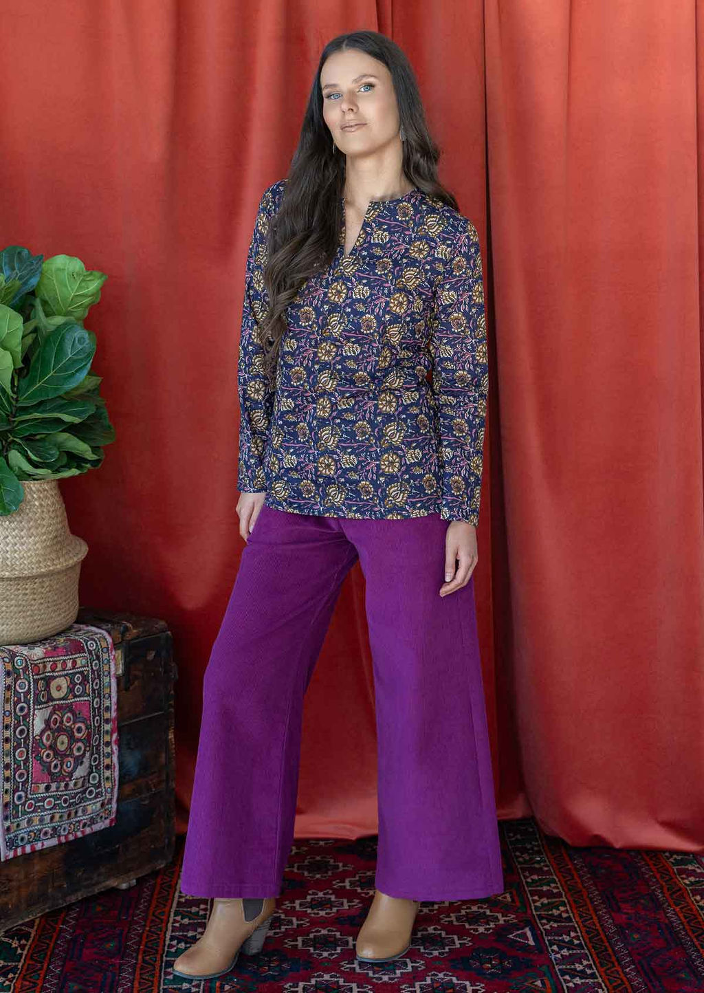 Model wears long sleeve shirt top with round neckline and V cutout, paired beautifully with plum corduroy pants.