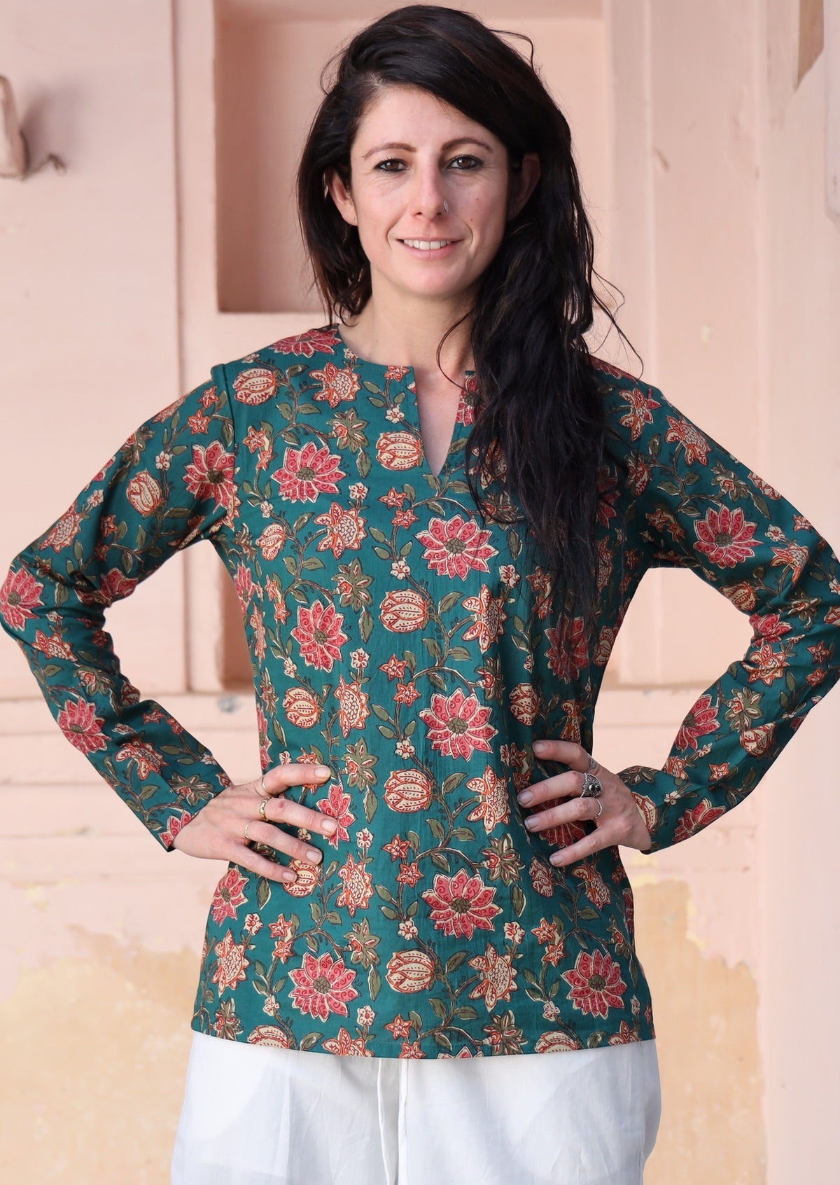 Woman wears cotton long sleeve top with keyhole V-cutout, in a green based floral print with hands on hips