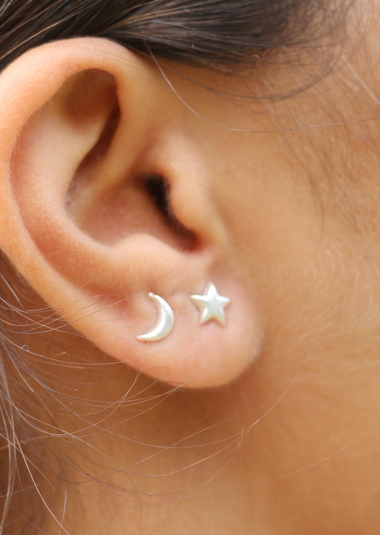 Woman wearing a pair of silver stud earrings, one designed with a crescent moon and the other with a star