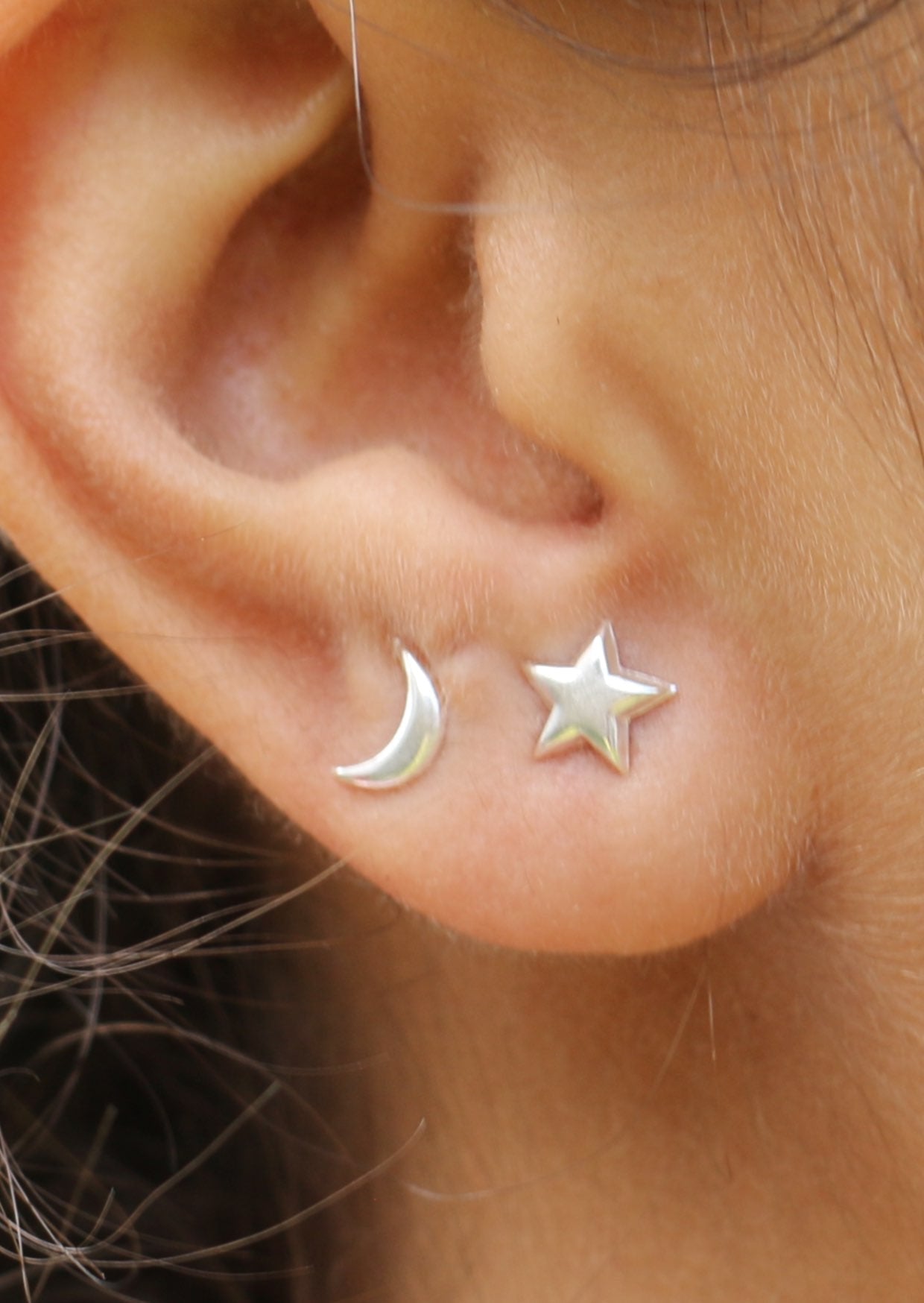 Close-up of an ear wearing star and moon silver studs with silver butterfly backs