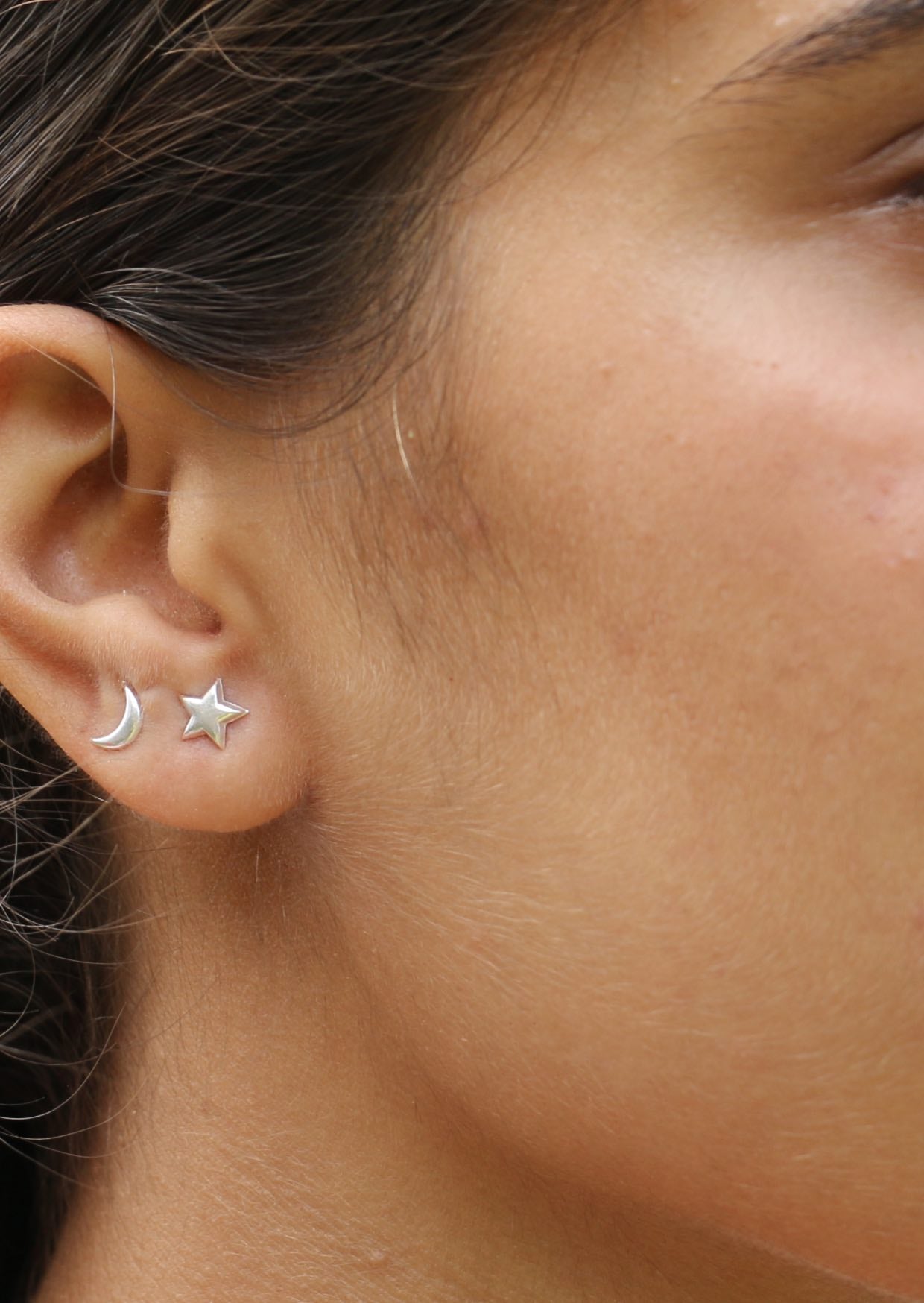 A close up of an ear adorned with delicate crescent moon and star silver studs with secure butterfly backs