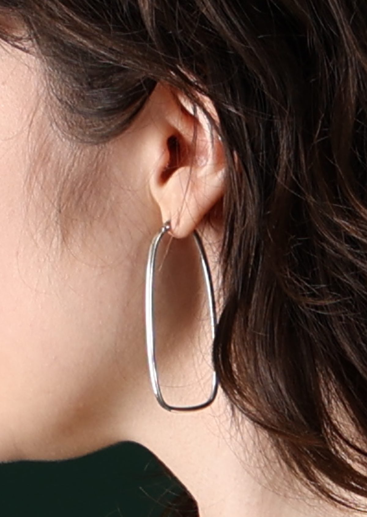 Model with dark hair wearing elongated large sterling silver hoop earrings