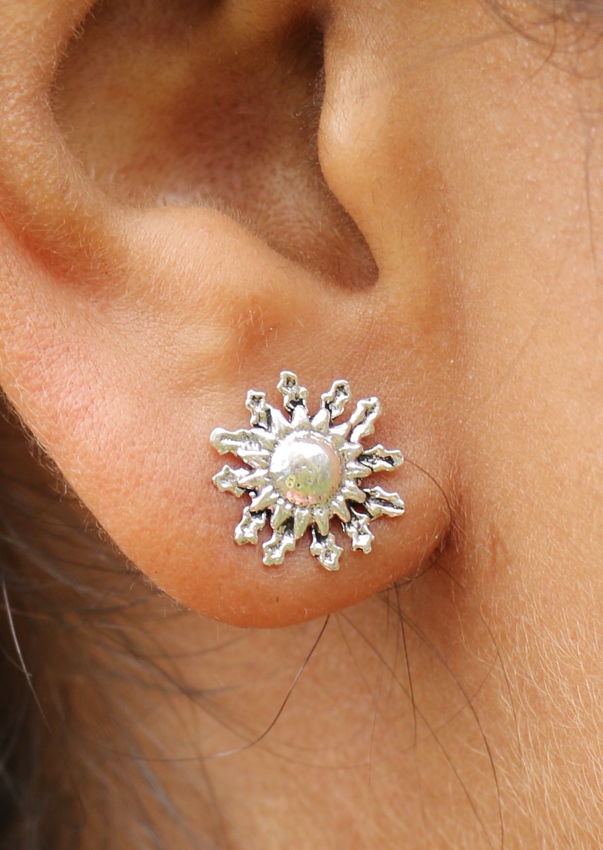 Silver sun-shaped small stud earrings with butterfly backs worn on a woman's ear