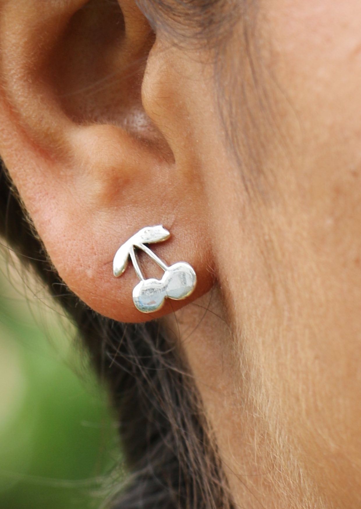 Close-up of an ear wearing silver cherry shaped studs with secure butterfly backs