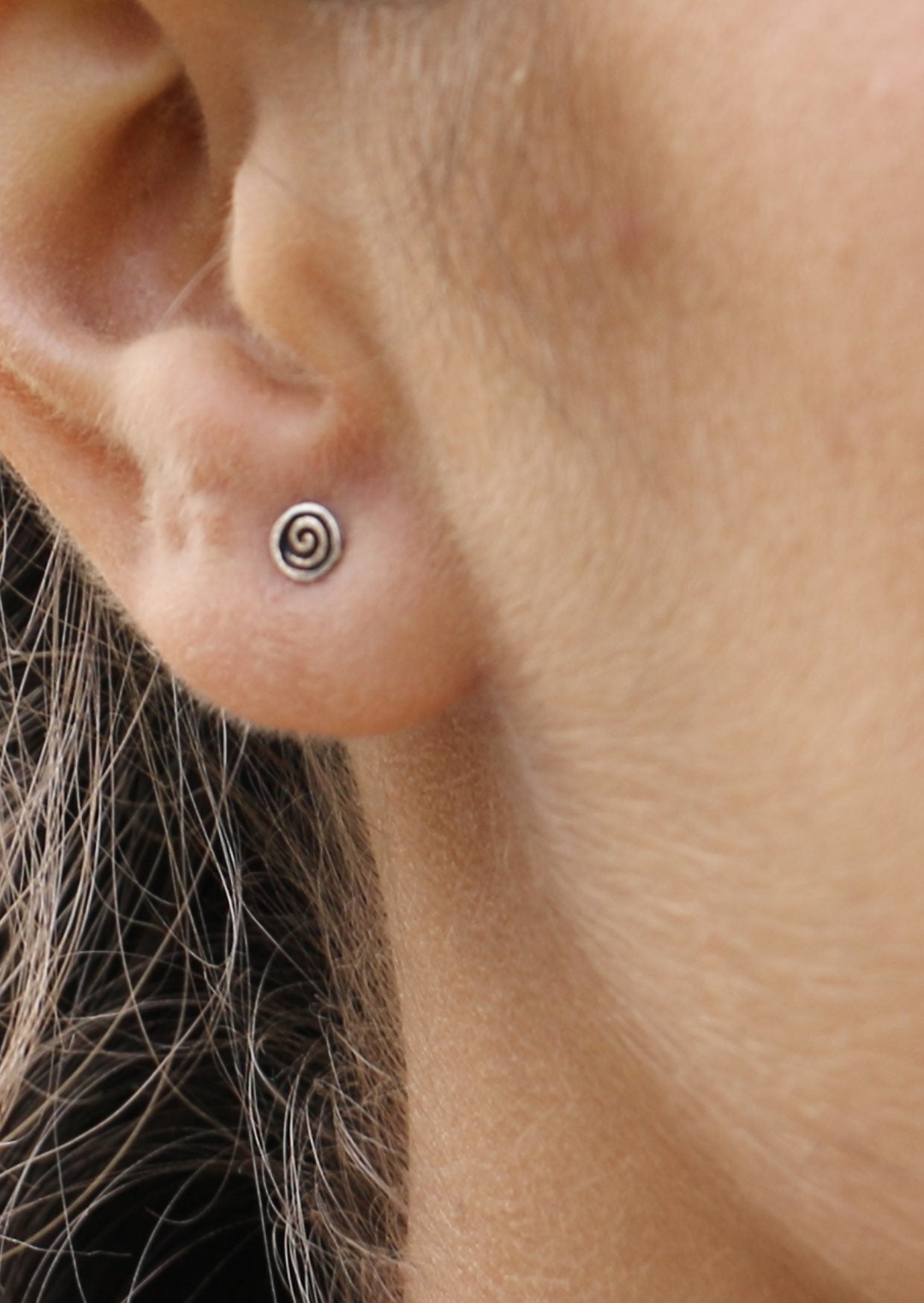 Close-up of an ear with a small silver disk studs and swirl imprinted on the front