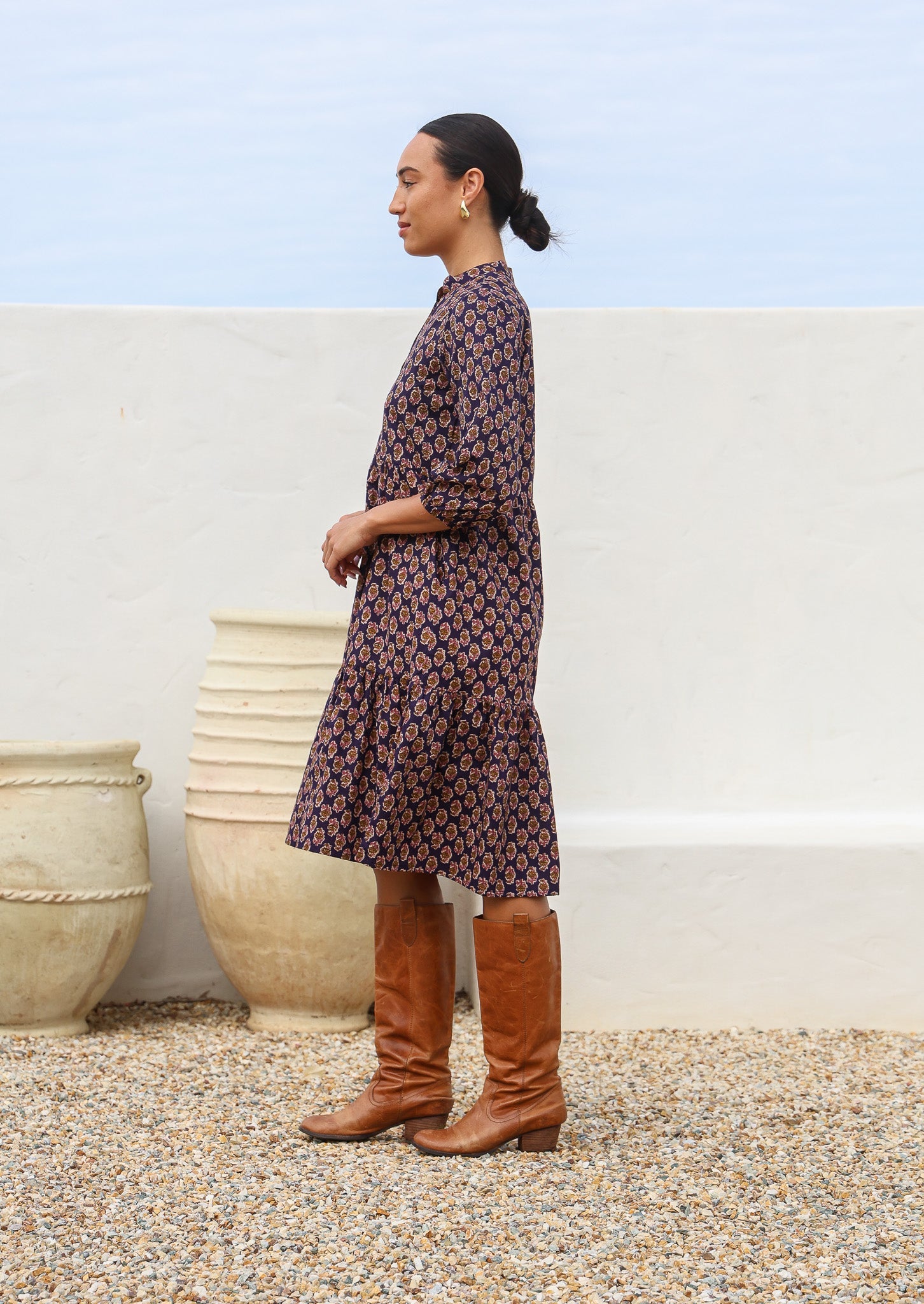 Woman stands side on in cotton relaxed fit tiered over the knee length dress with hidden side pockets