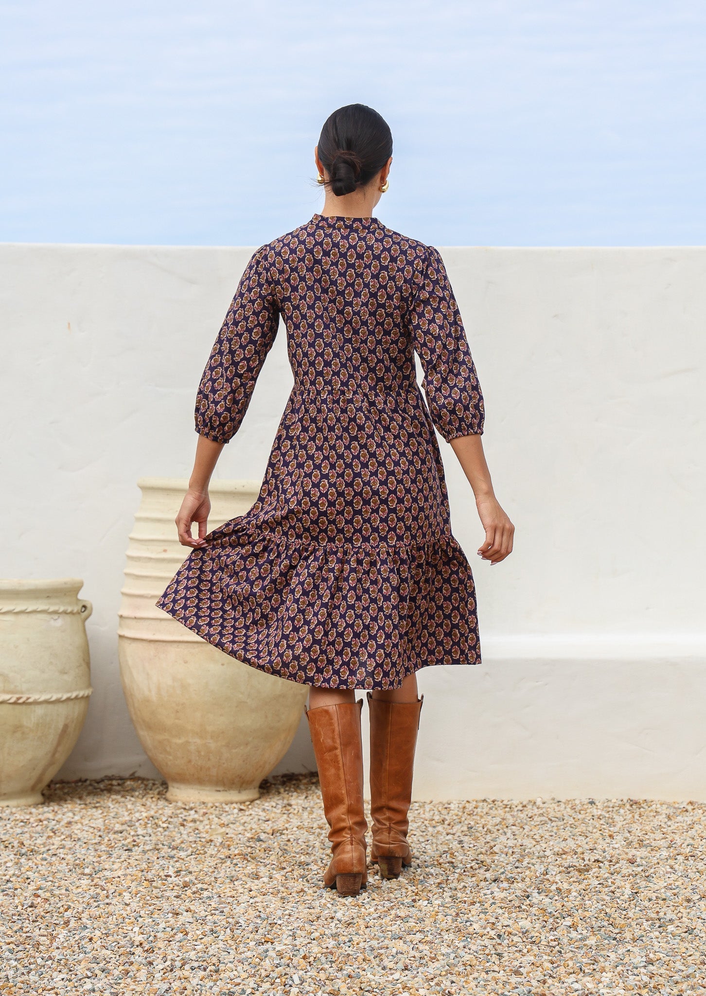 Back of woman in cotton tiered dress with 3/4 sleeves in a floral motif on a dark purple base
