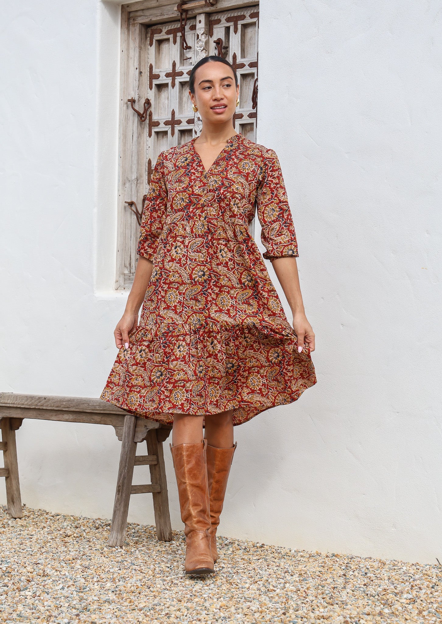 Model walks in cotton tiered over the knee floral print dress, holding the skirt out, paired with tan boots
