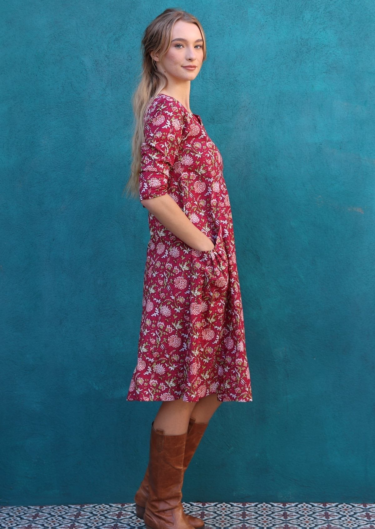 Model wears 100% knee length cotton dress with hints of pink, white and green on red base