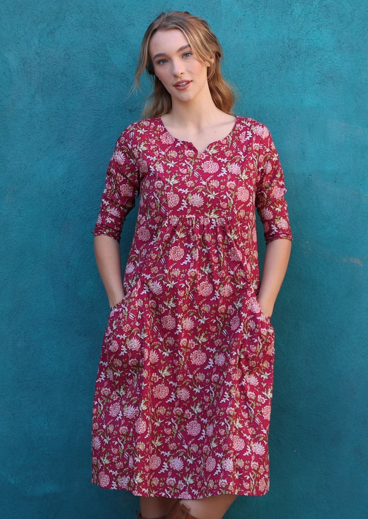 Model wearing 100% cotton dress with beautiful floral print in pink, green and white on bright red base.