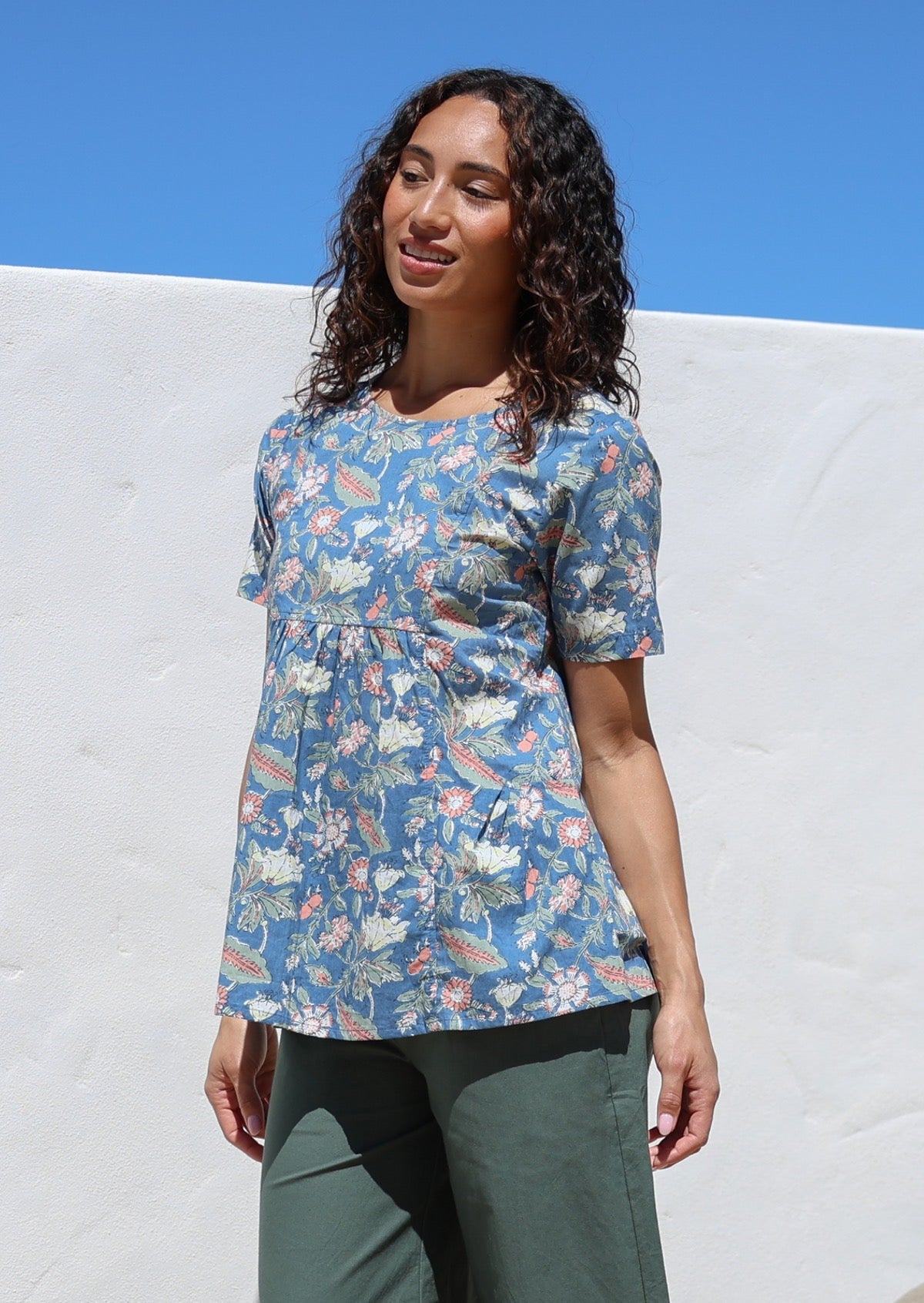 Woman wearing a relaxed fit 100% cotton top in a dusty blue based floral print with short sleeves, pockets and gathers under the bust