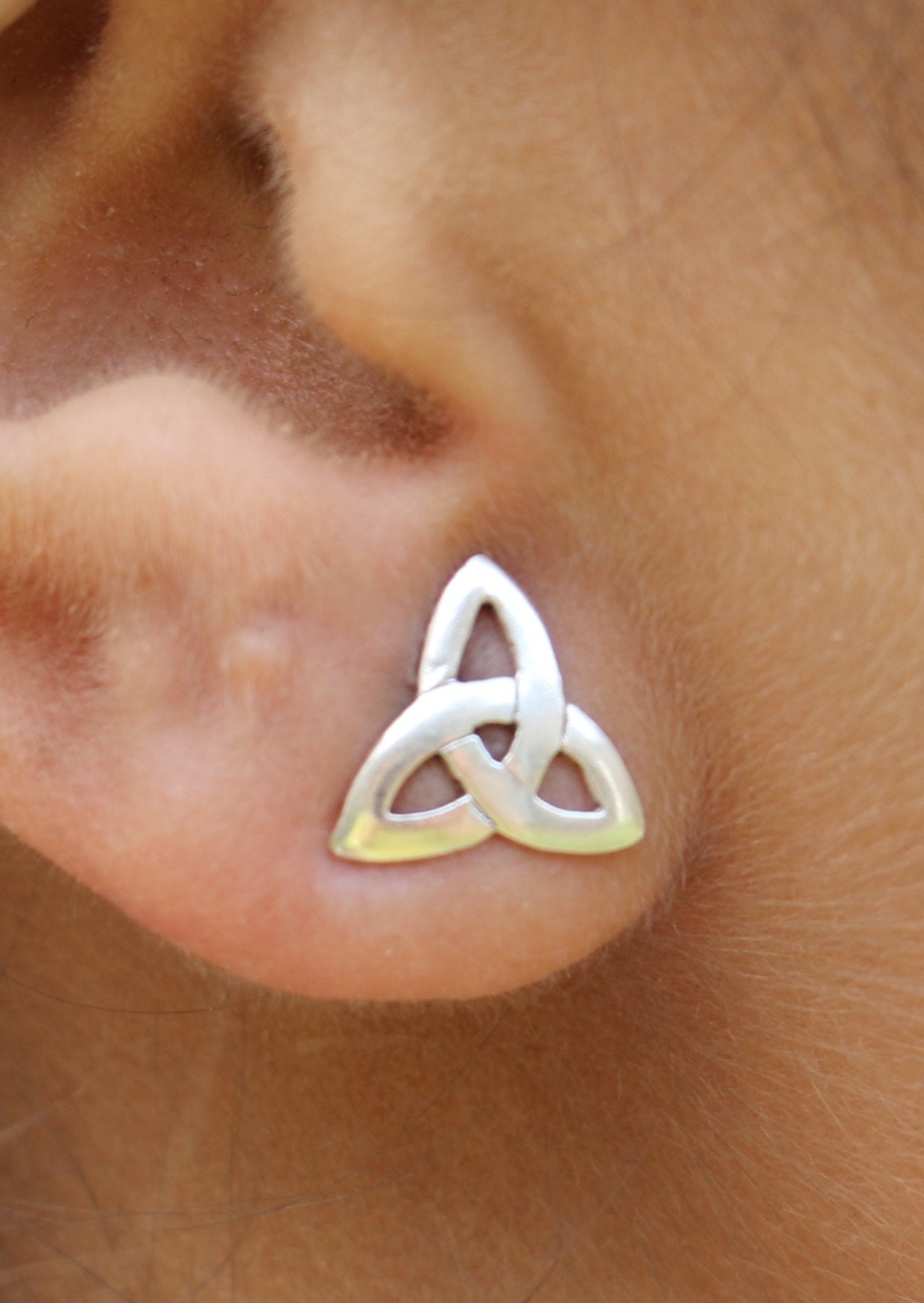 Three pointed silver trinity knot studs on a person's ear