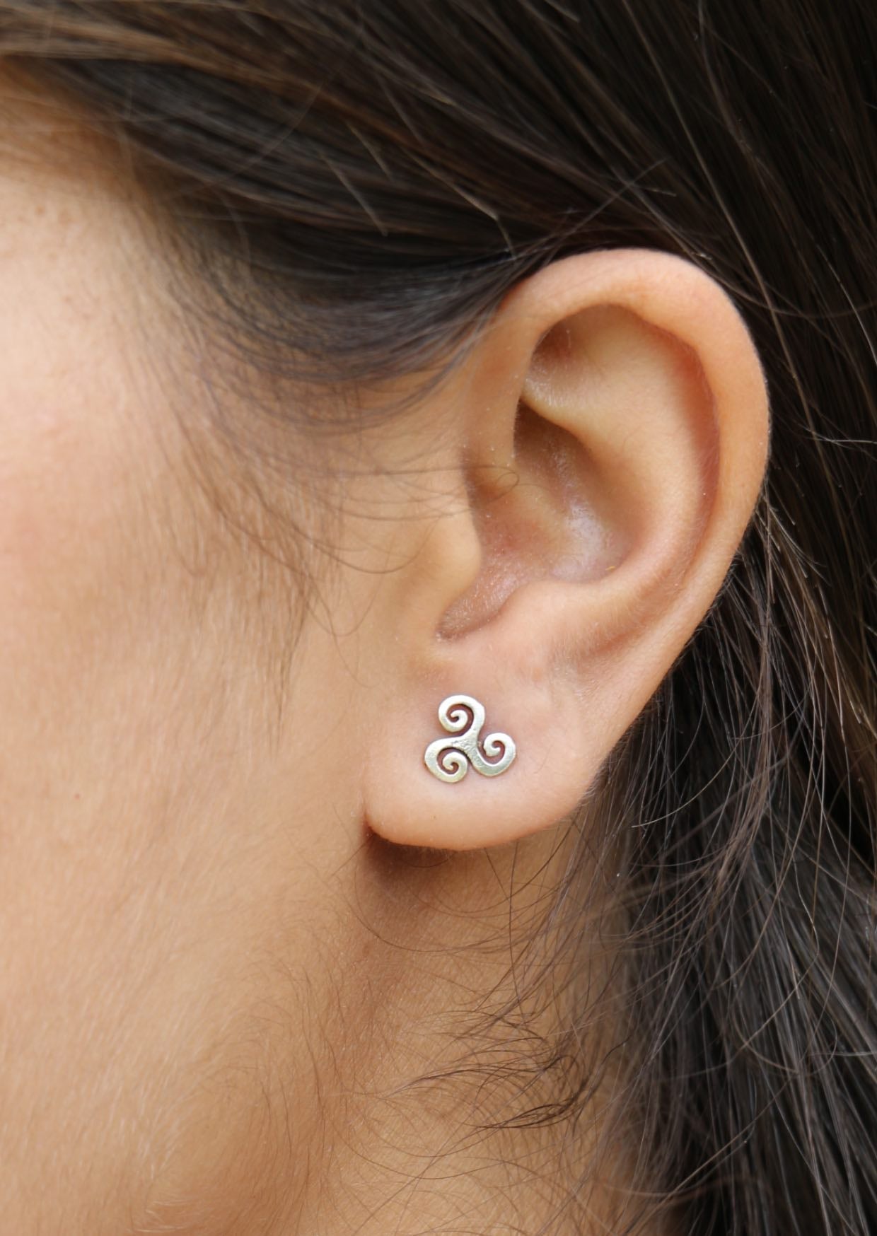 Close-up of an ear wearing a silver triskele stud earring with three repeating spirals joined at the center