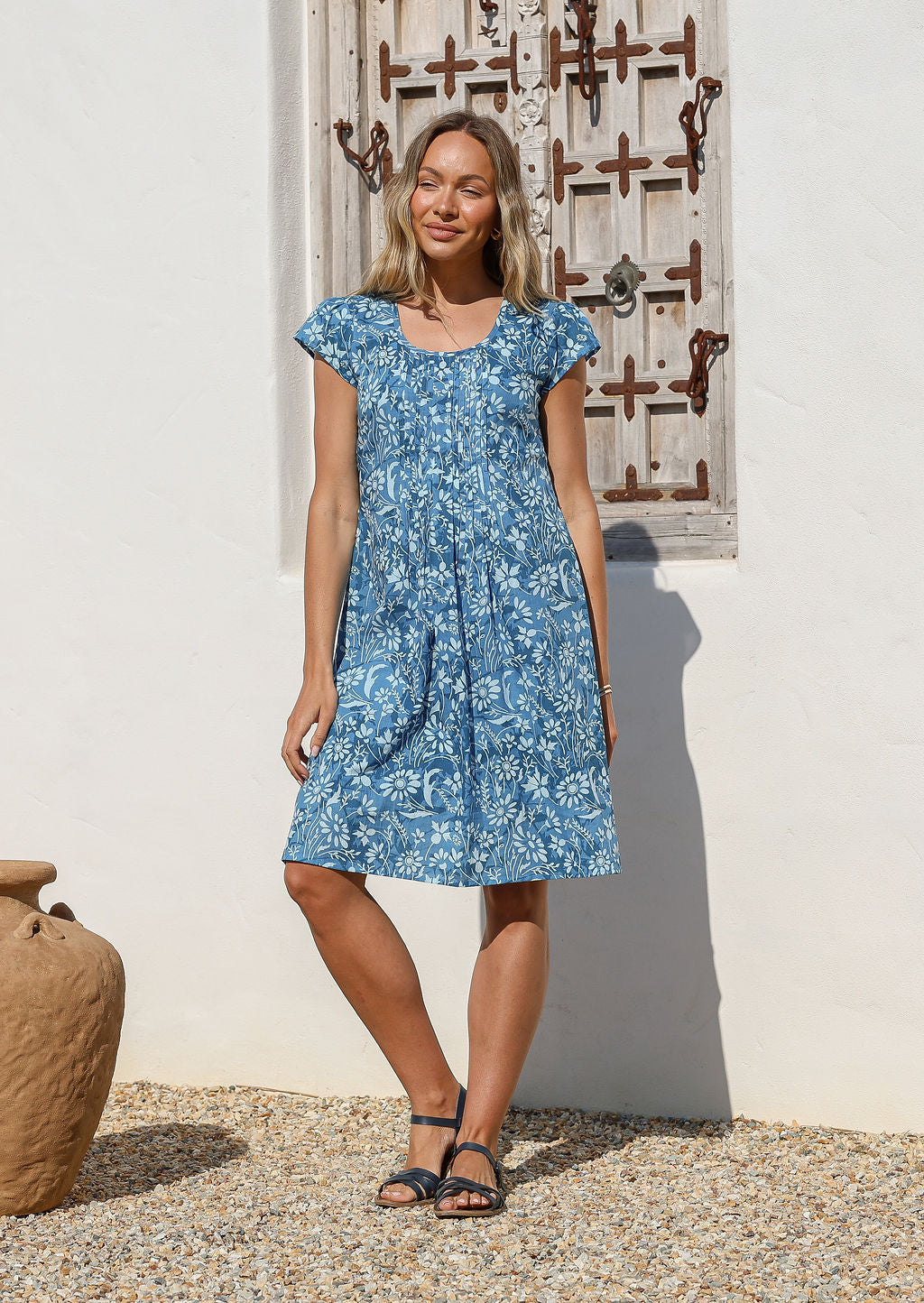 Woman wearing a blue floral cotton knee length dress with cap sleeves and a round neckline