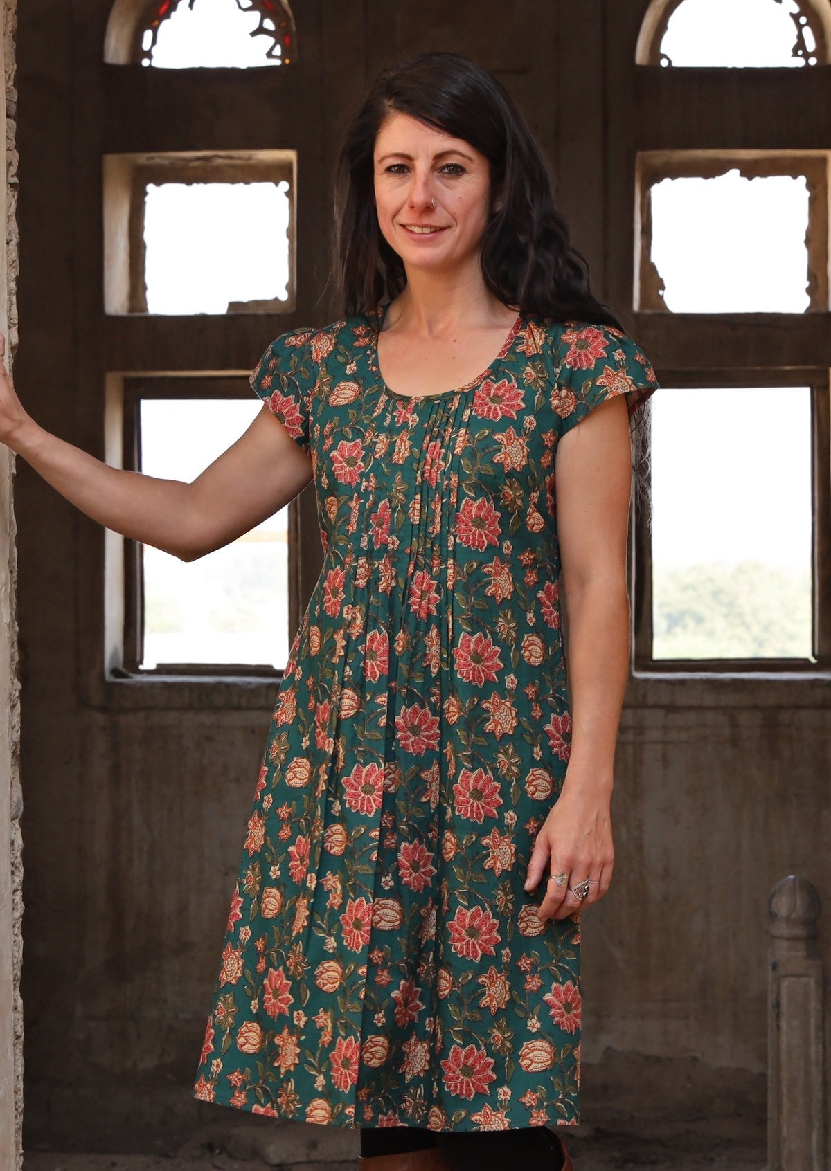 Women wearing a short sleeves cotton dress with pleated design and floral print on a dark green based dress.