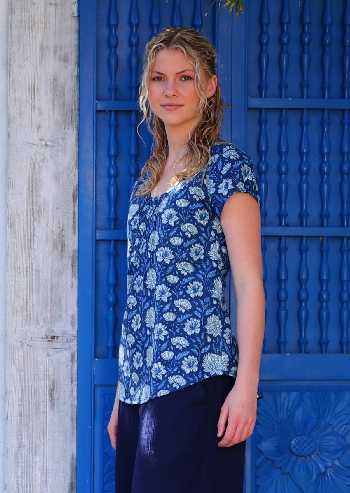 Model standing in front of blue door wearing 100 percent cotton navy floral blouse with scoop neck