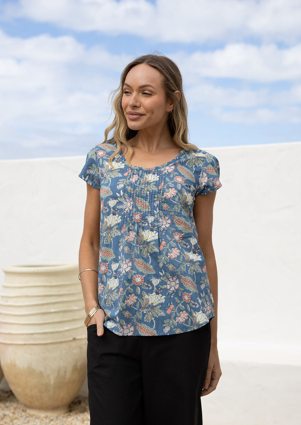 Woman wearing a blue floral short sleeve top with scoop round neckline and pleated detail across the bodice