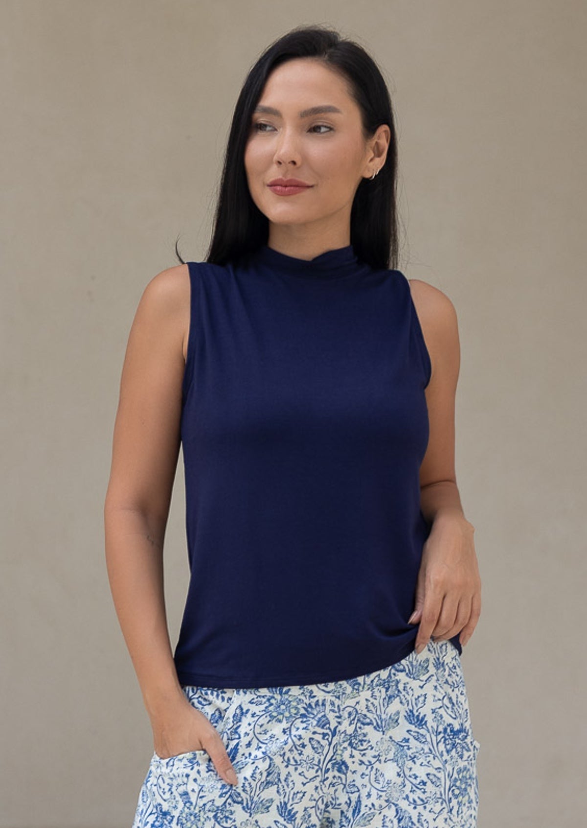 Woman wearing a navy sleeveless top with floral pants against a beige background