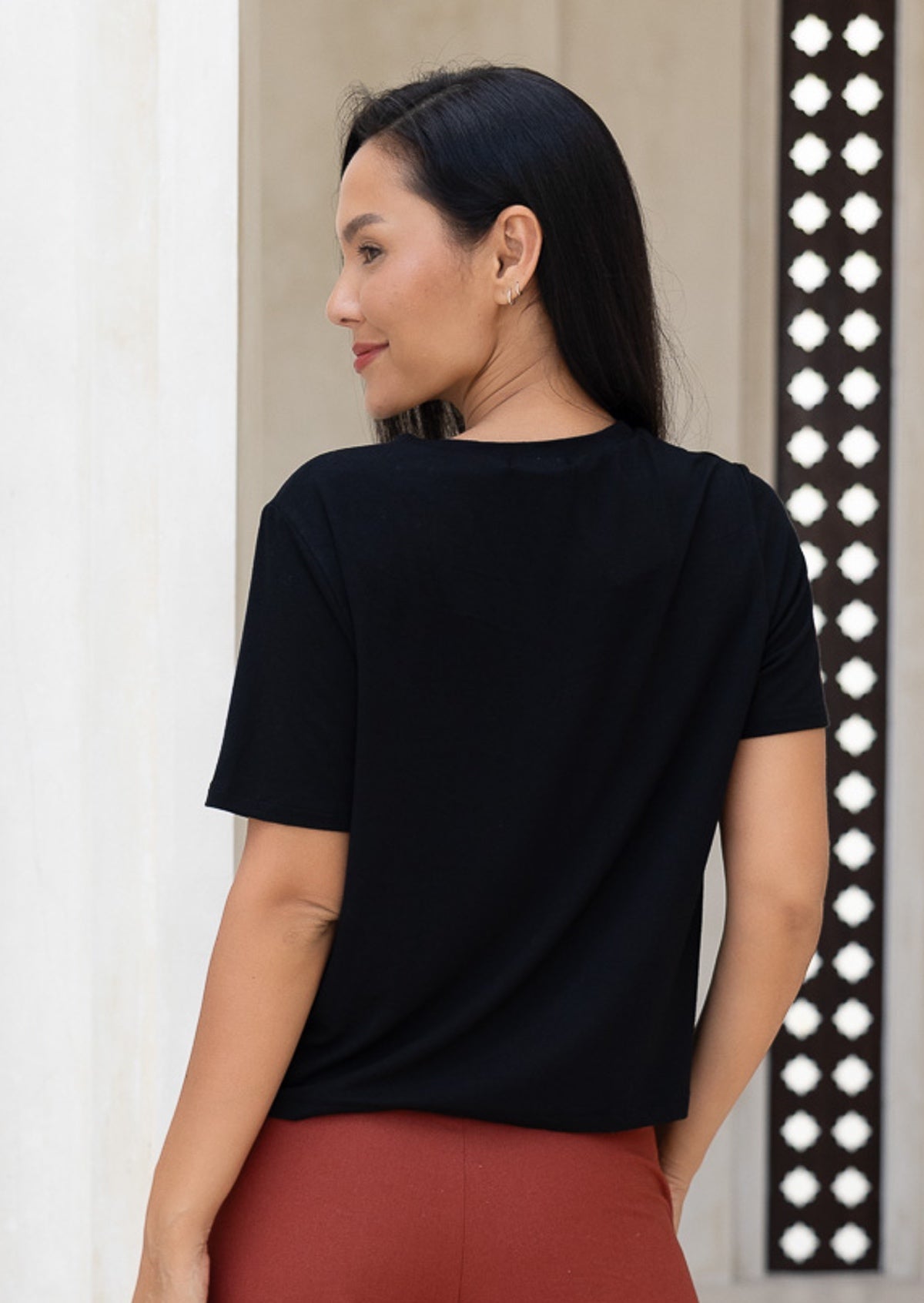Back view of woman wearing a black short sleeve top and rust pants