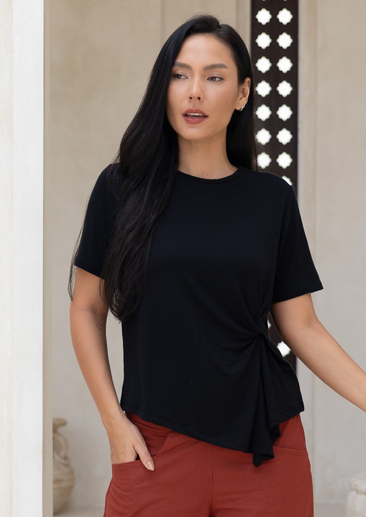 Woman wearing a black stretch rayon top with short sleeves paired with rust pants