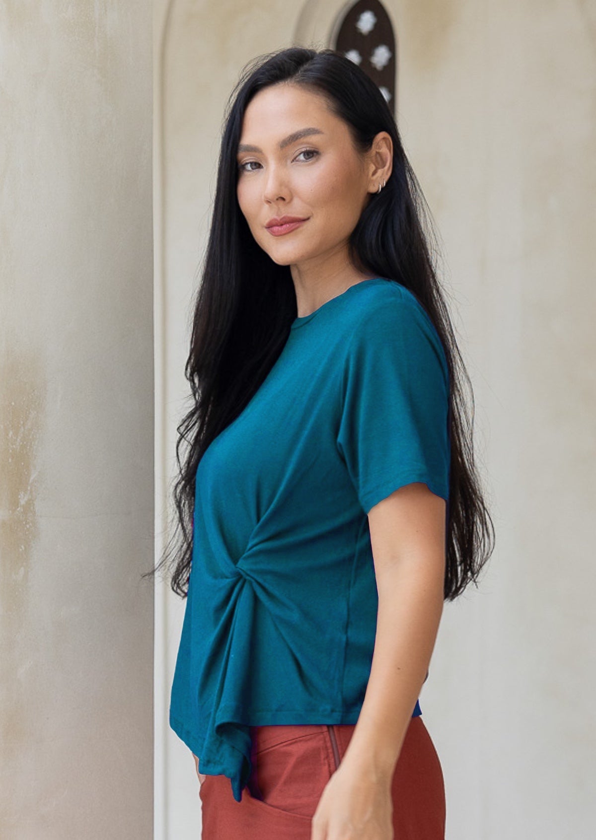 Woman stands side on wearing a teal rayon short sleeve t-shirt with a knot detail