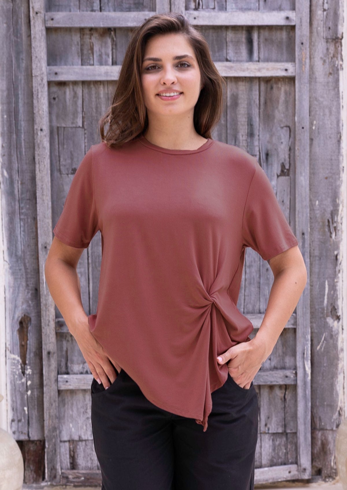 Woman wearing a terracotta short sleeve rayon top and black pants with hand in pockets
