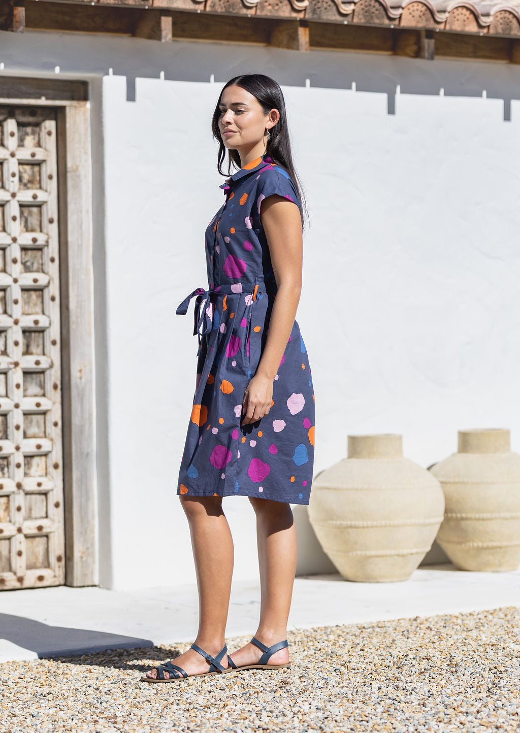 Woman wearing an abstract print cotton knee length dress with cap sleeves and a waist tie standing outdoors